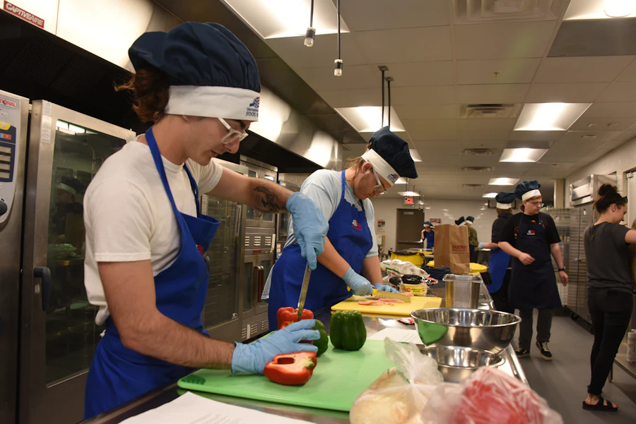 Cooks in aprons and caps chopping vegetables in a large commercial kitchen