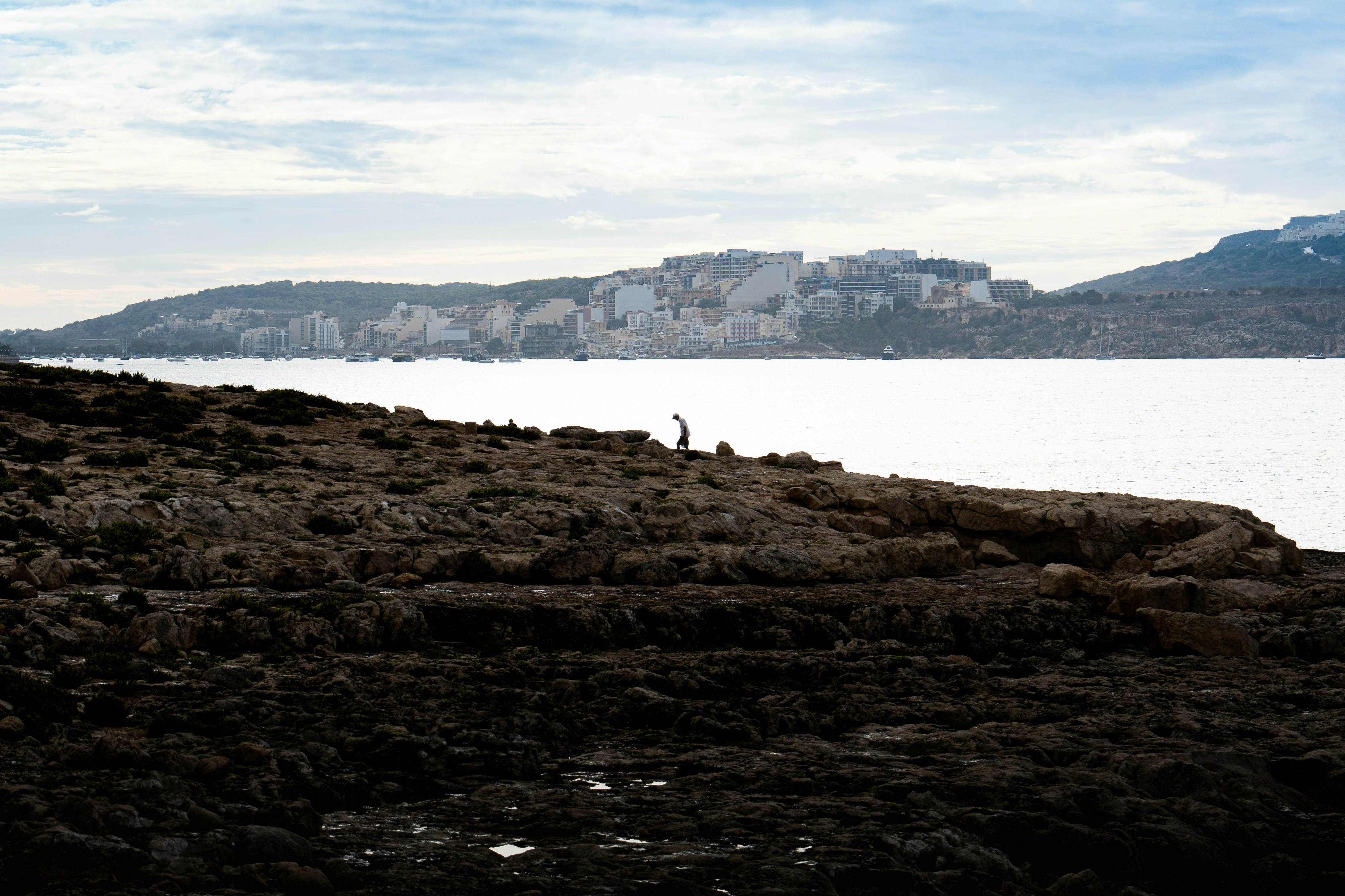 A person standing on top of a rocky hill next to a body of water