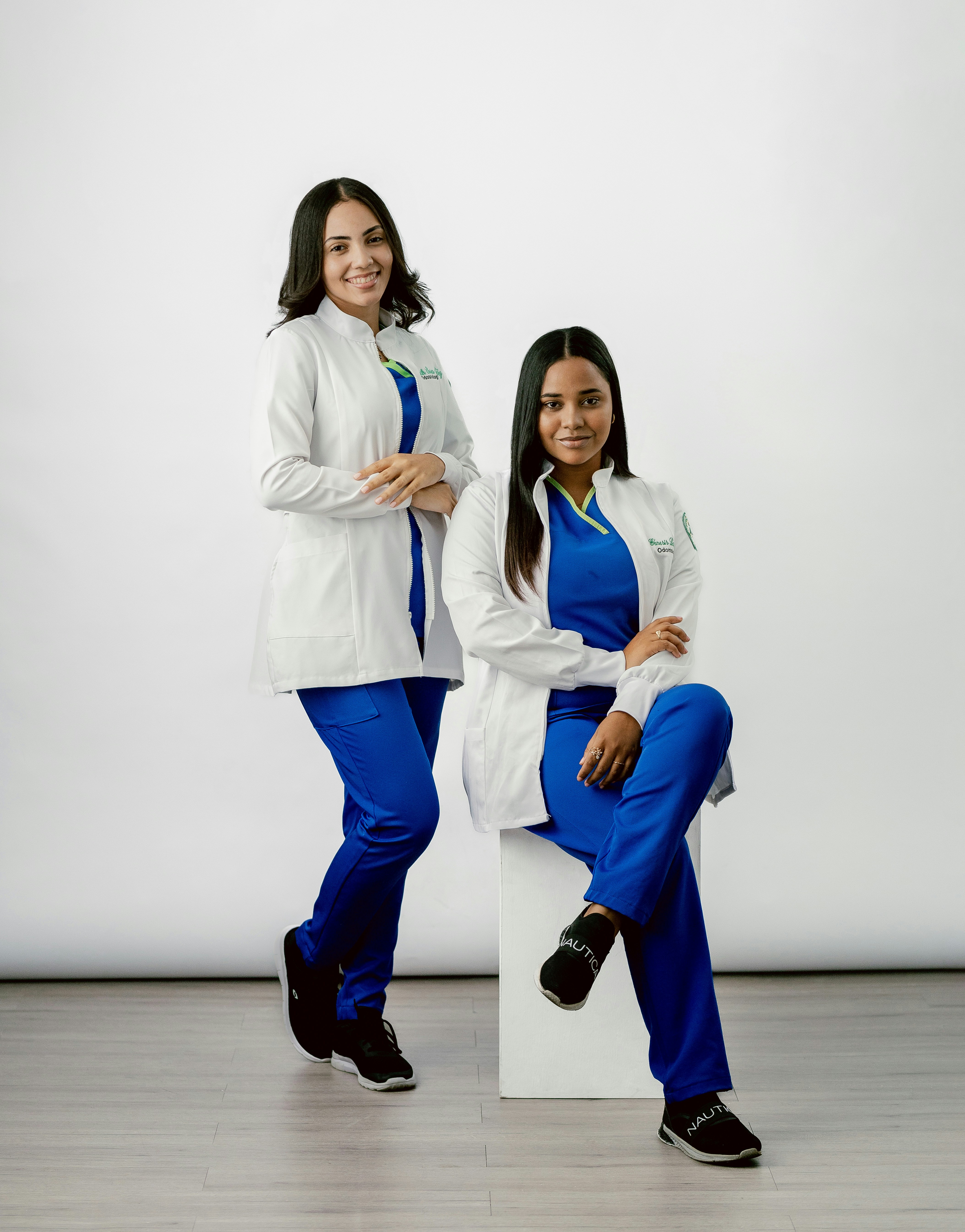 Two women are posing for a picture in front of a white background