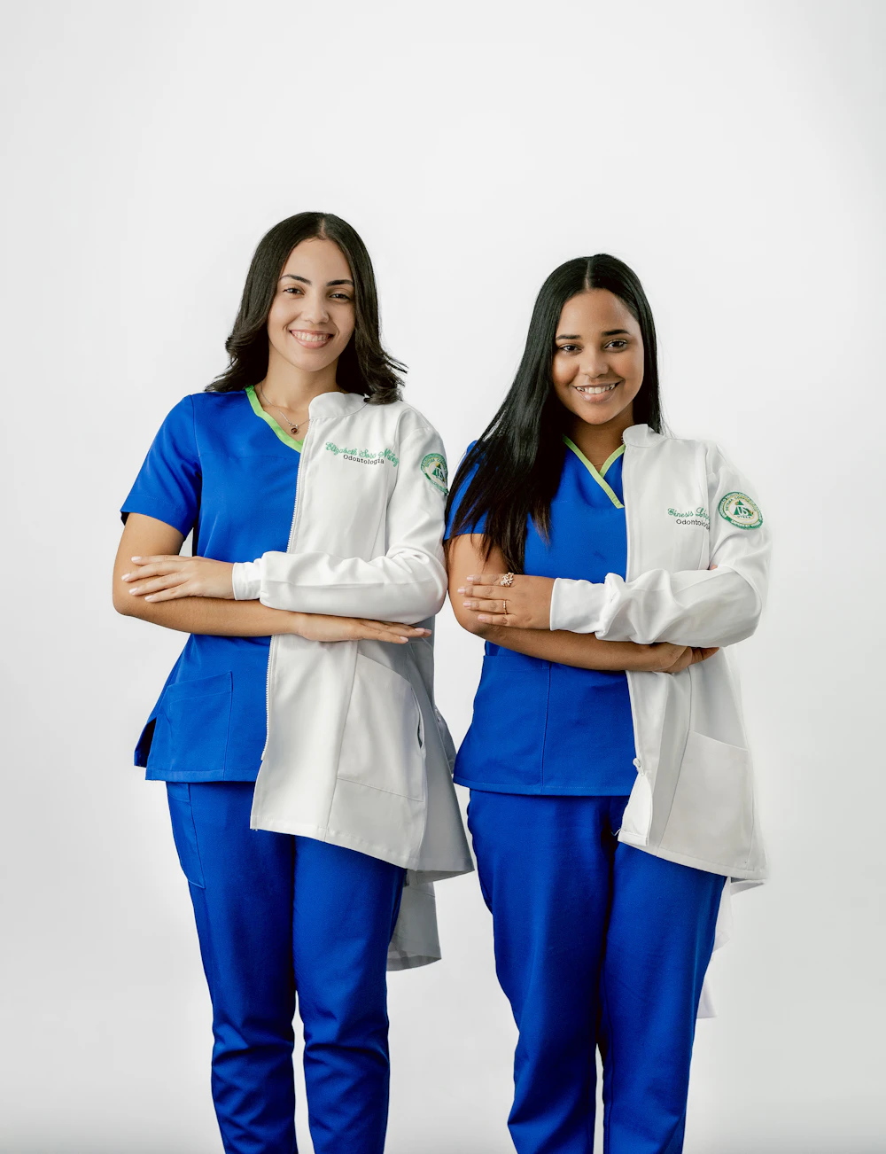 Two young registered nurses in scrubs and white coats, smiling