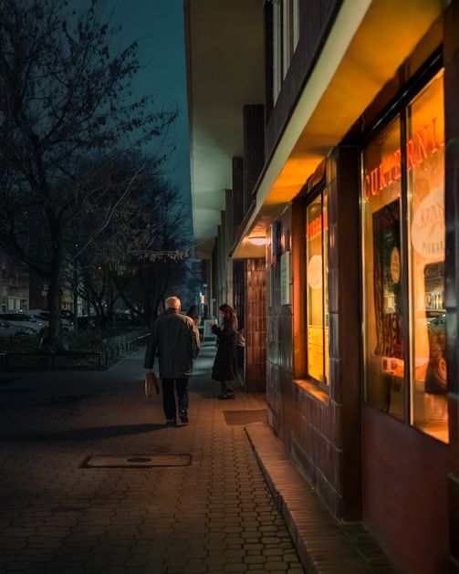 A couple of people walking down a sidewalk next to a store