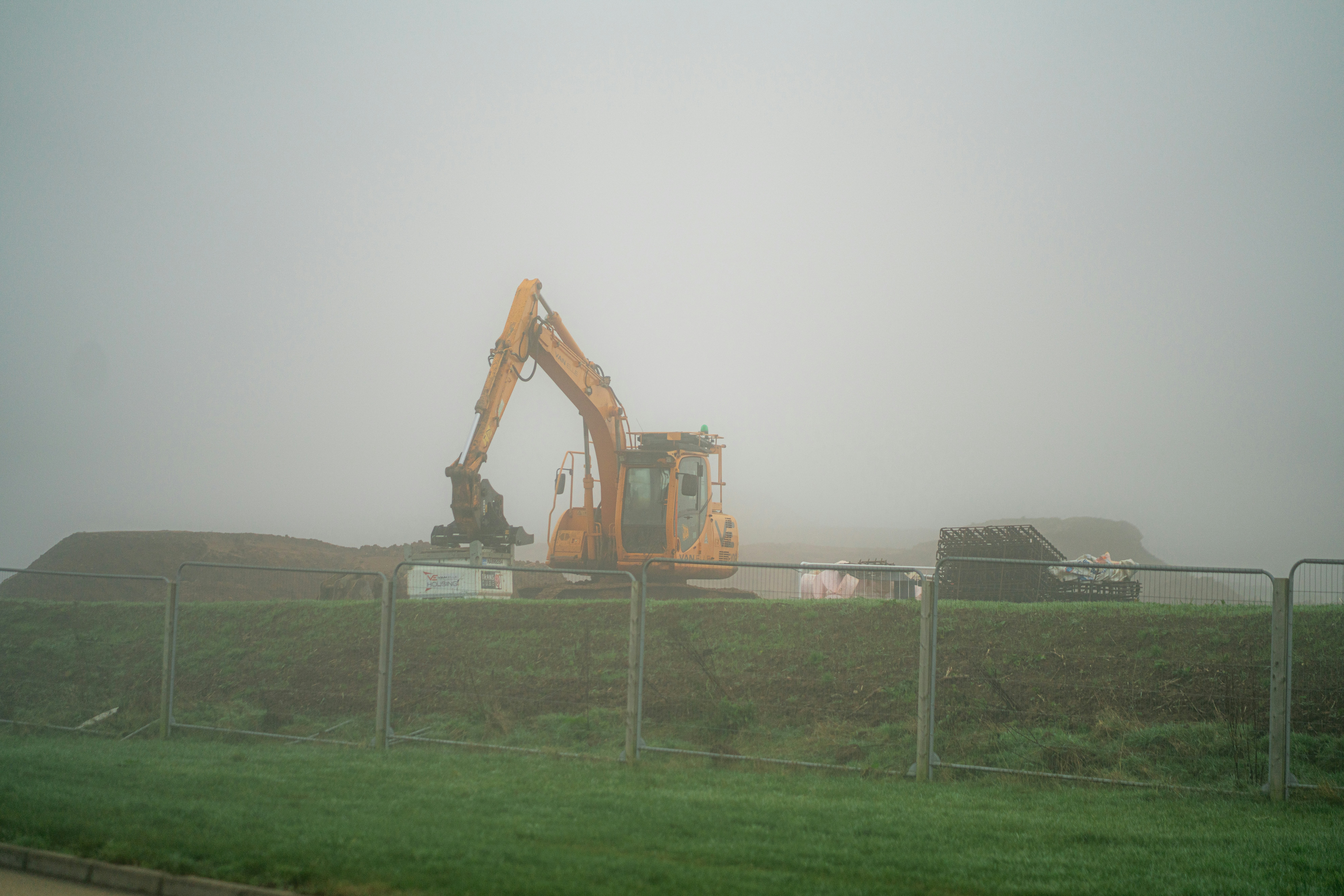 A tractor is parked behind a fence on a foggy day