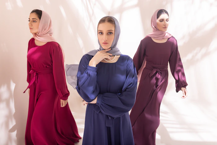 Three women in jewel-toned abayas and hijabs standing together.
