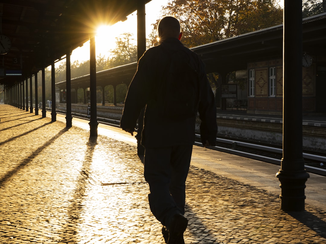 A man walking down a sidewalk next to a train station,