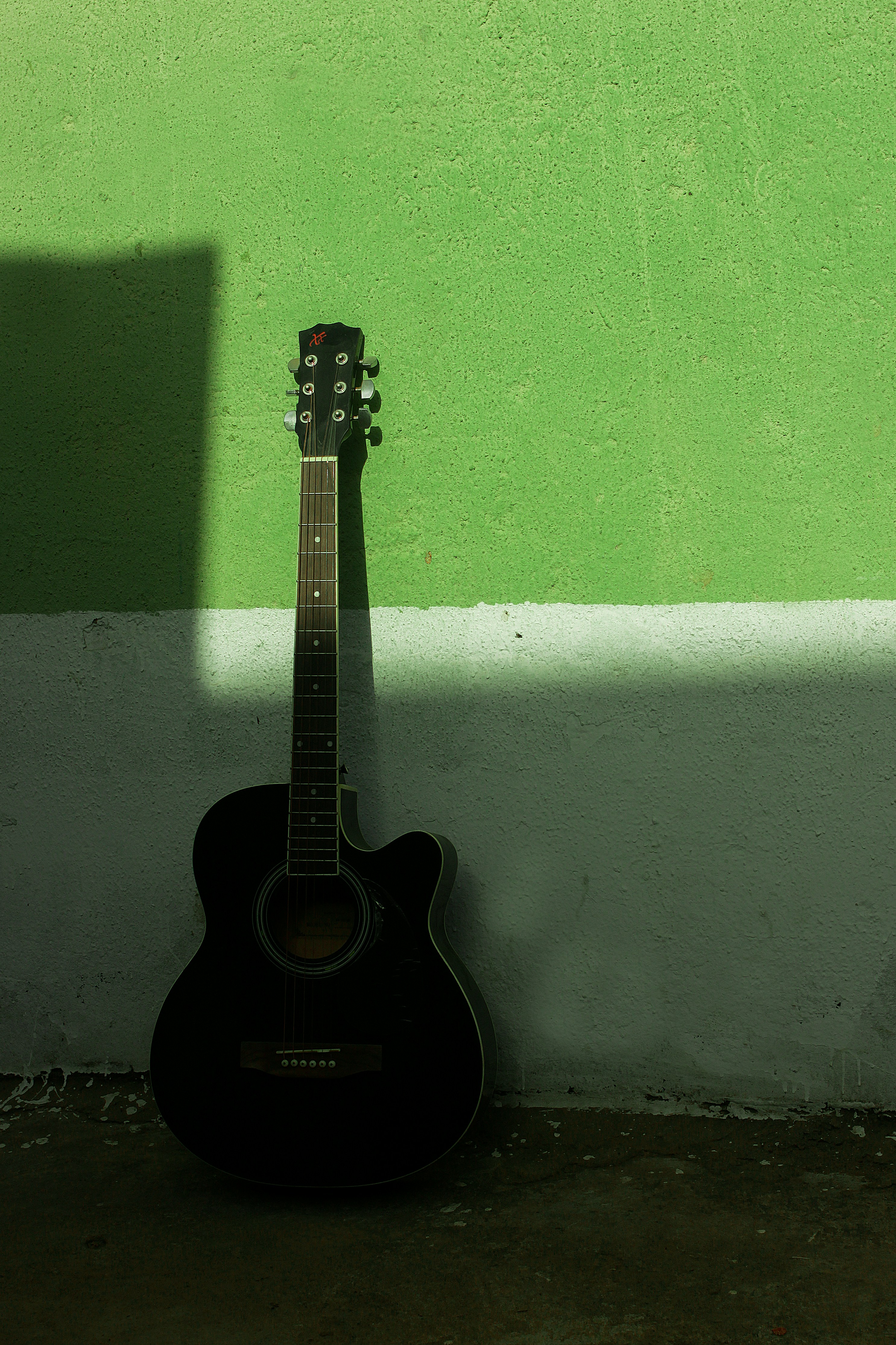 A black guitar leaning against a green wall