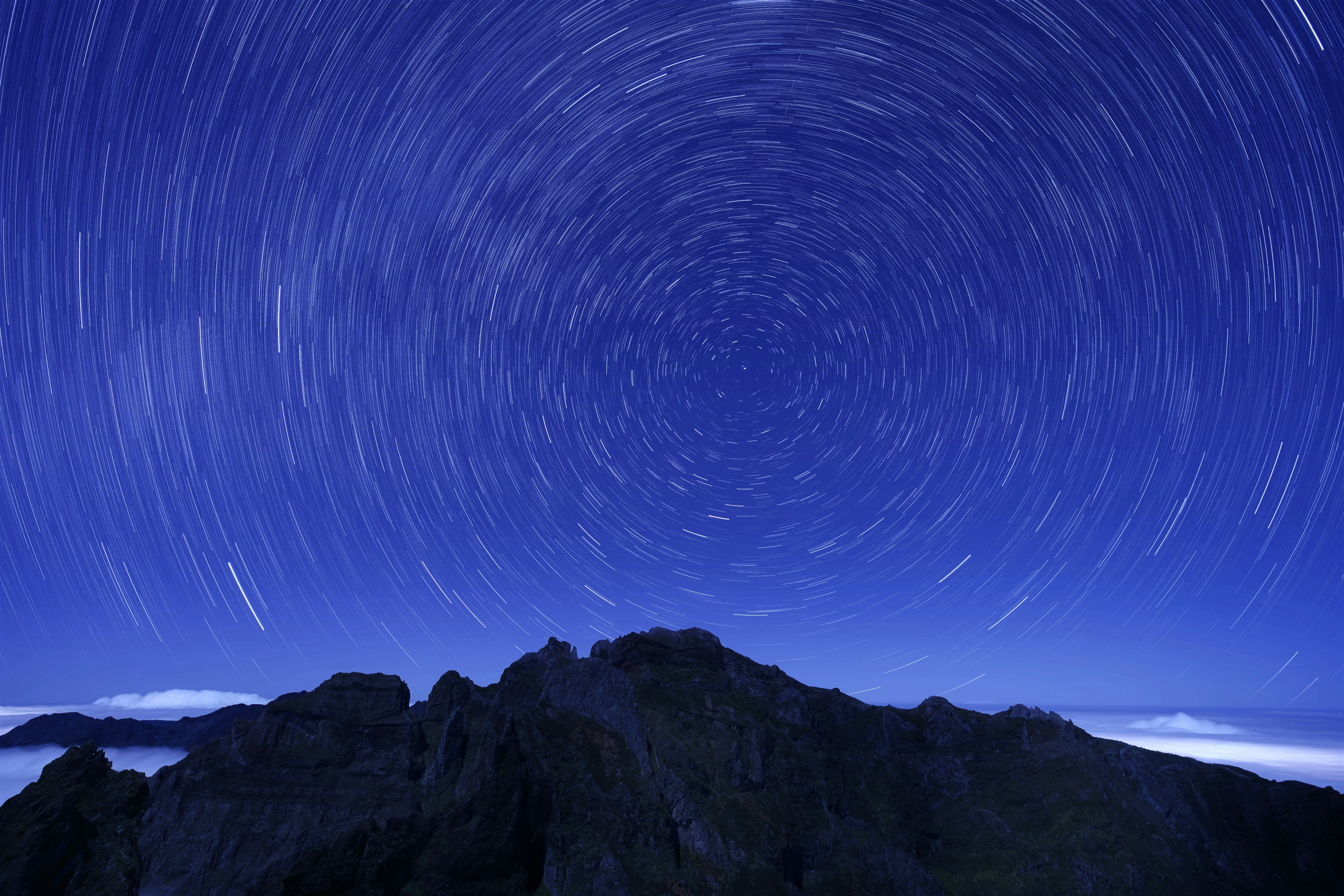 Gece vakti gökyüzü ve koyu renkli dağlar, gökyüzünde halka şeklinde beliren mistik şekillerle birlikte.