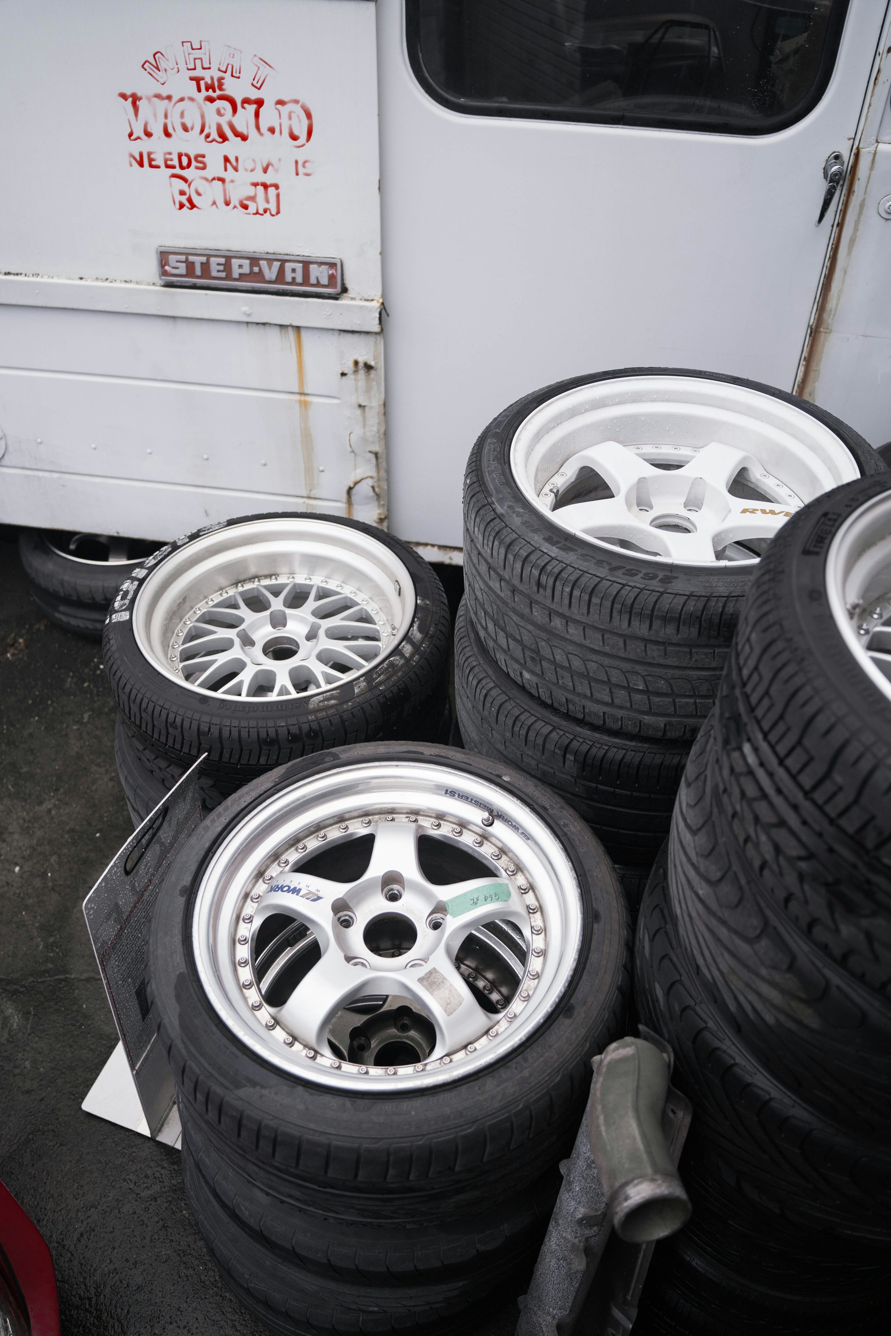 A pile of tires and rims sitting next to a truck