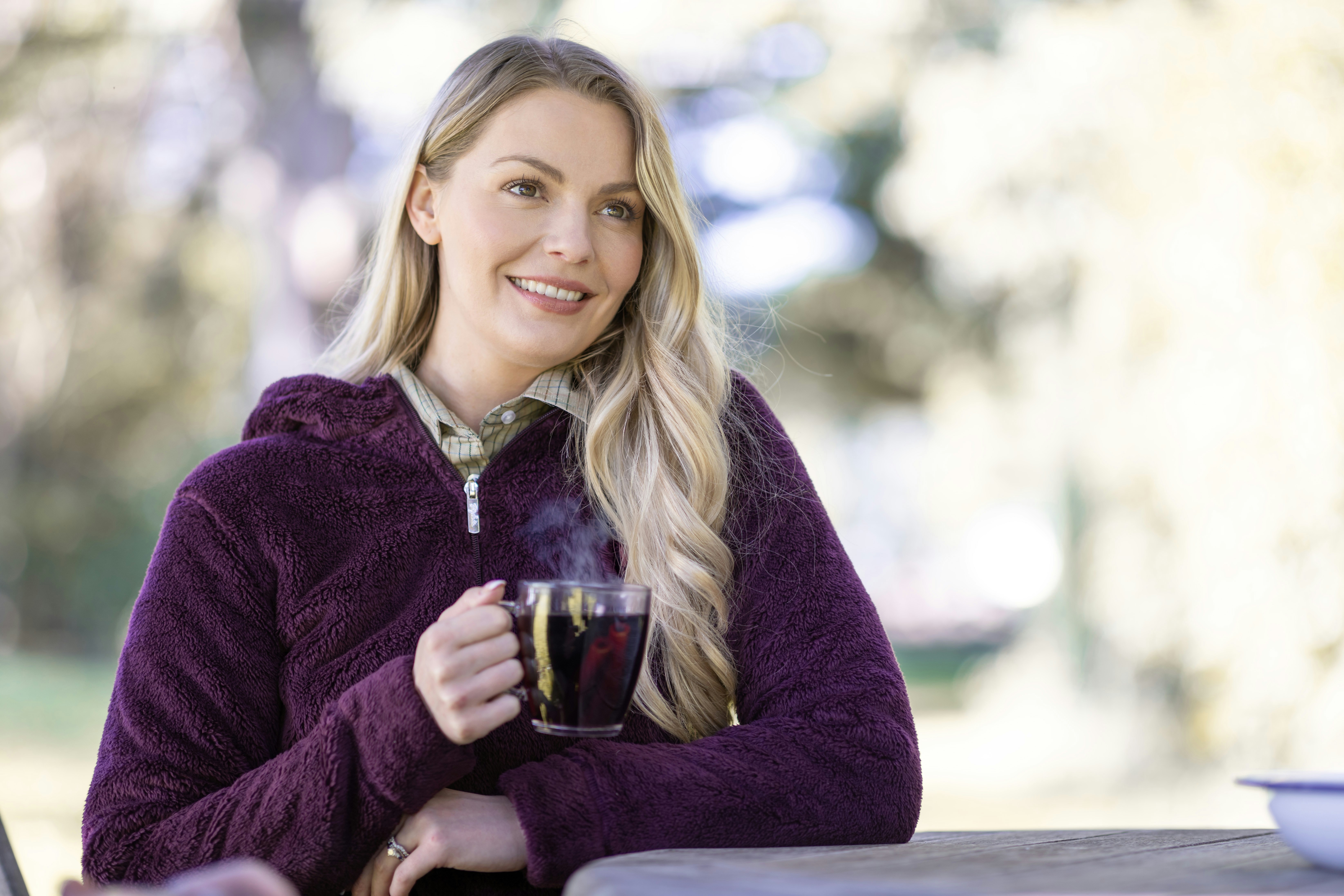 A woman wearing a purple fleece outside in the Yorkshire countryside as she enjoys a hot beverage