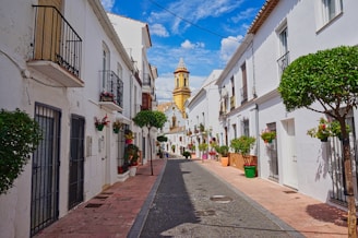 A narrow street lined with white buildings and trees