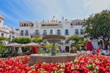 A fountain surrounded by red flowers in front of a white building