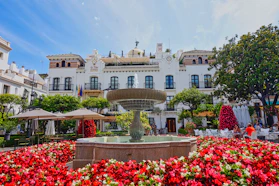 A fountain surrounded by red flowers in front of a white building