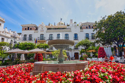 A fountain surrounded by red flowers in front of a white building