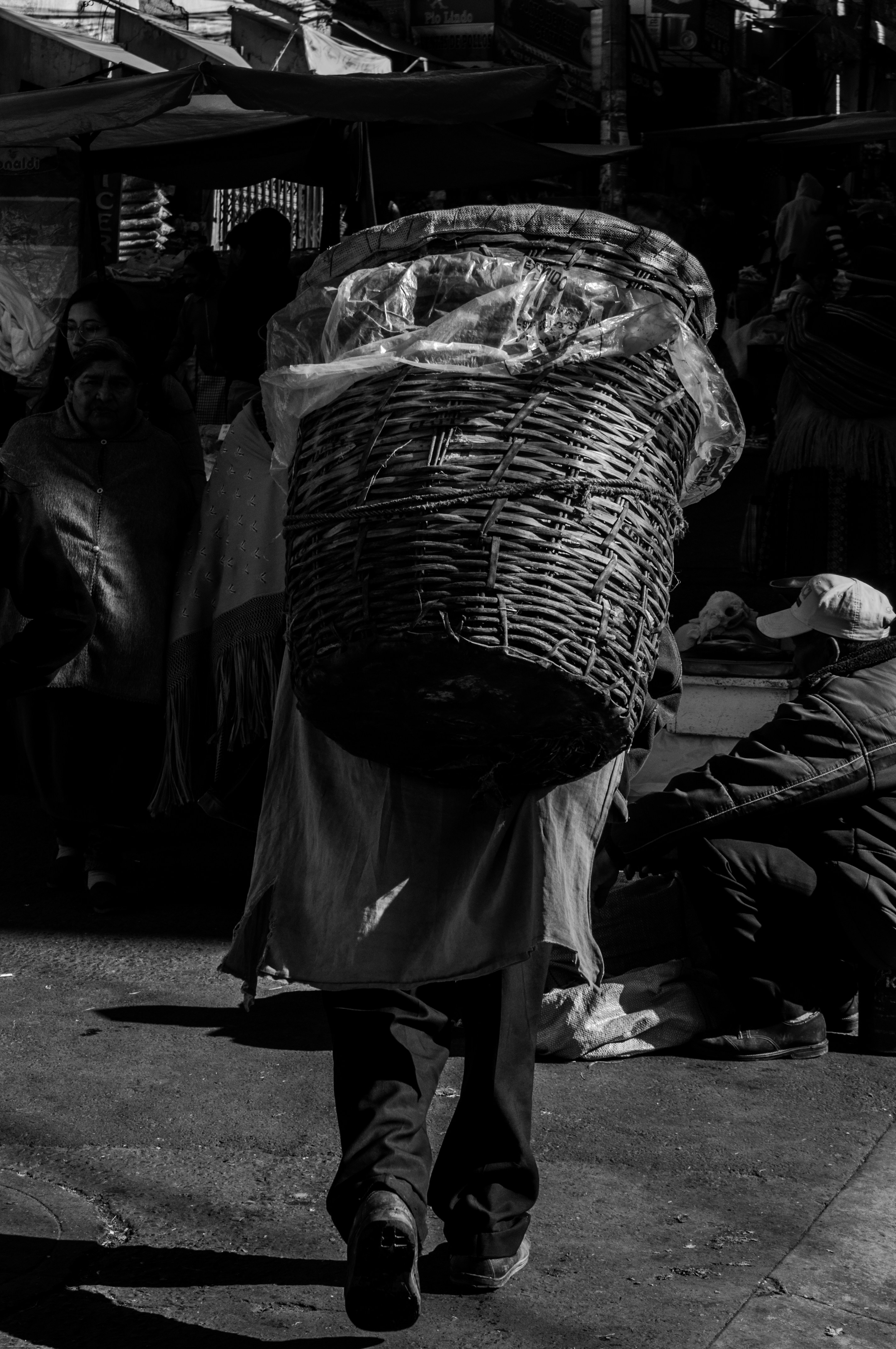 A black and white photo of a person carrying a basket