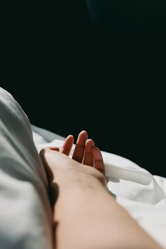 A person lying in bed with their hand out, representing recovery from a illness