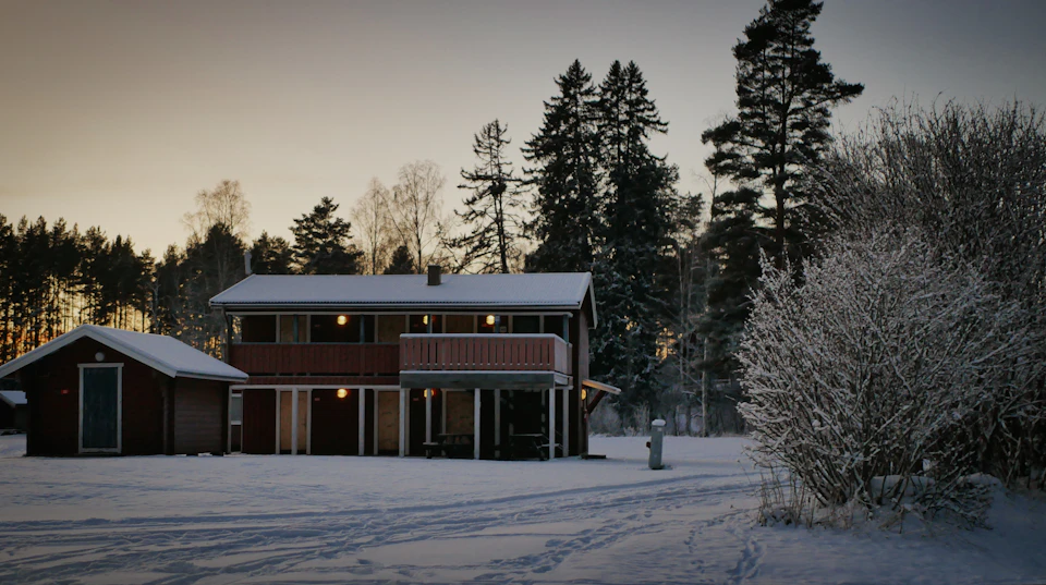 Two-story house with red roof set against a snowy landscape with surrounding trees