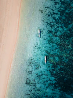 Two boats are in the water near a sandy beach