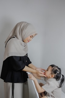 A woman helping a little girl put on a hijab