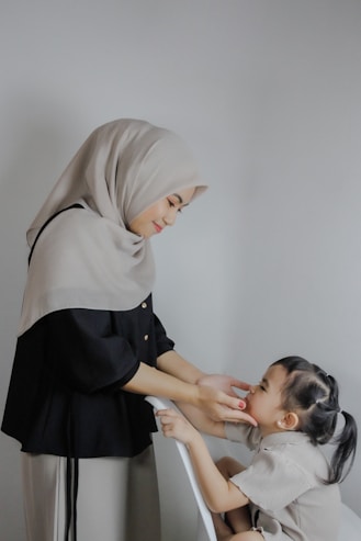 A woman helping a little girl put on a hijab