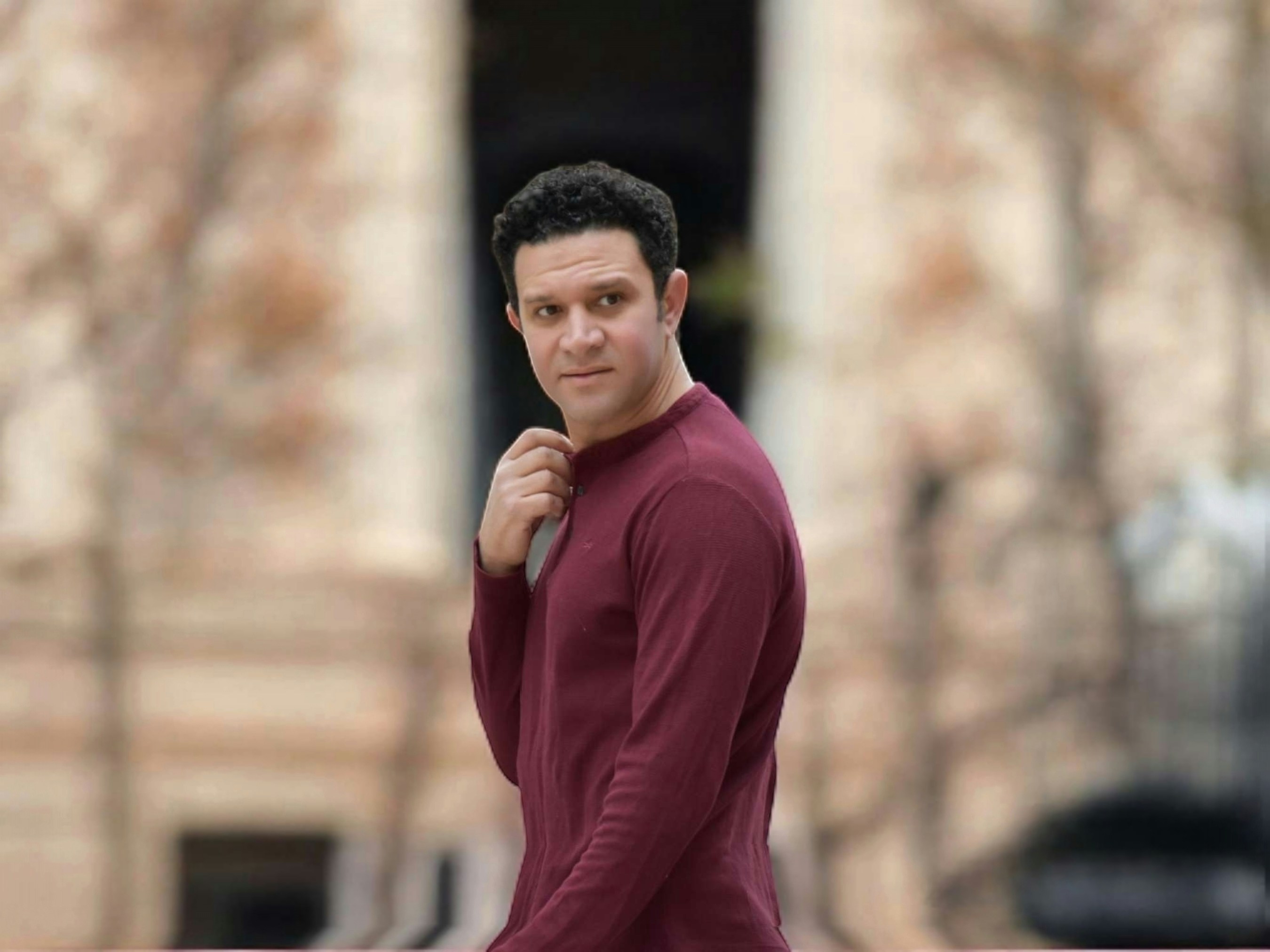 A man in a maroon shirt is walking in front of a building