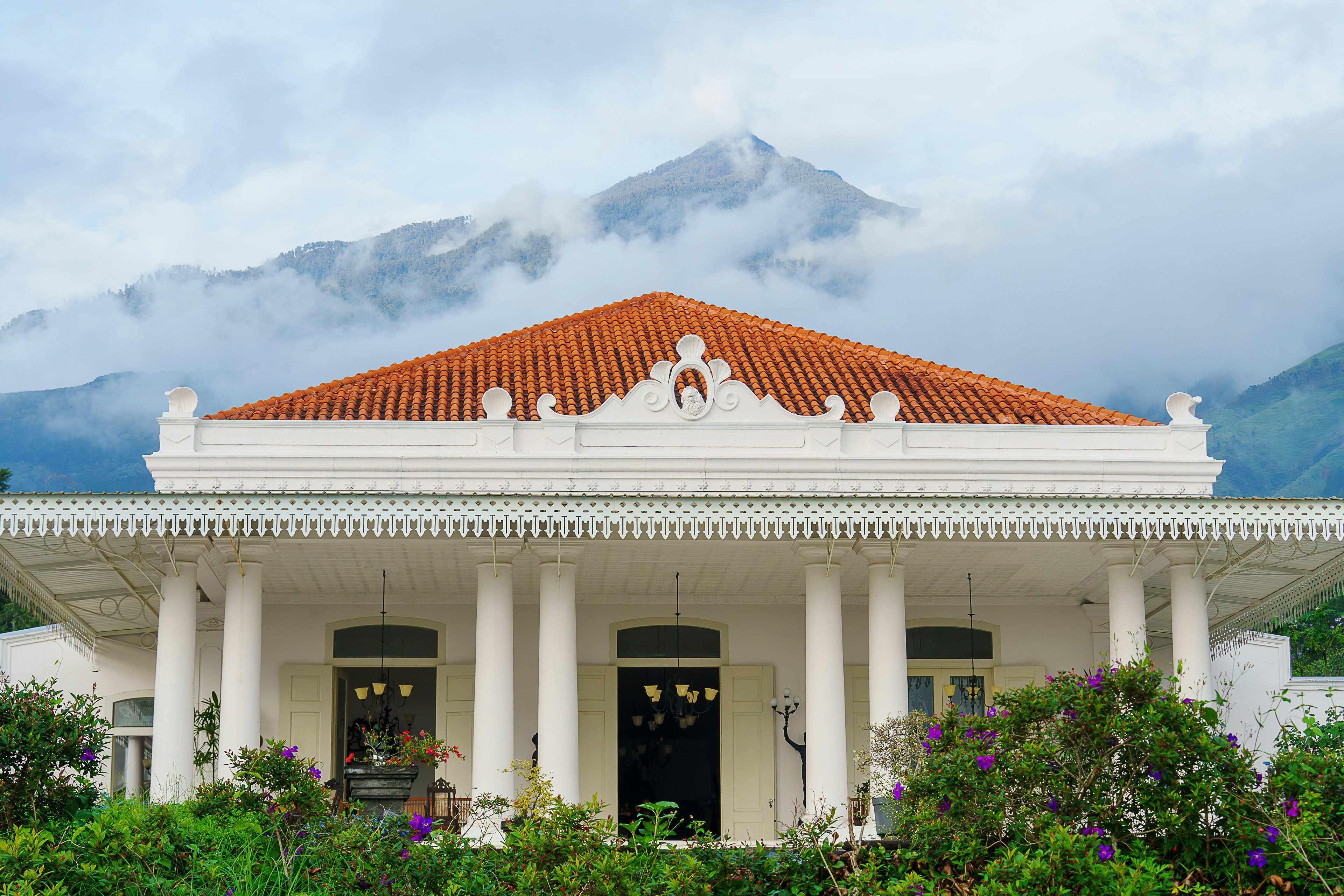 A white building with a red roof surrounded by greenery