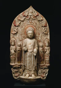 A carved stone buddha statue with attendants and decorative arch