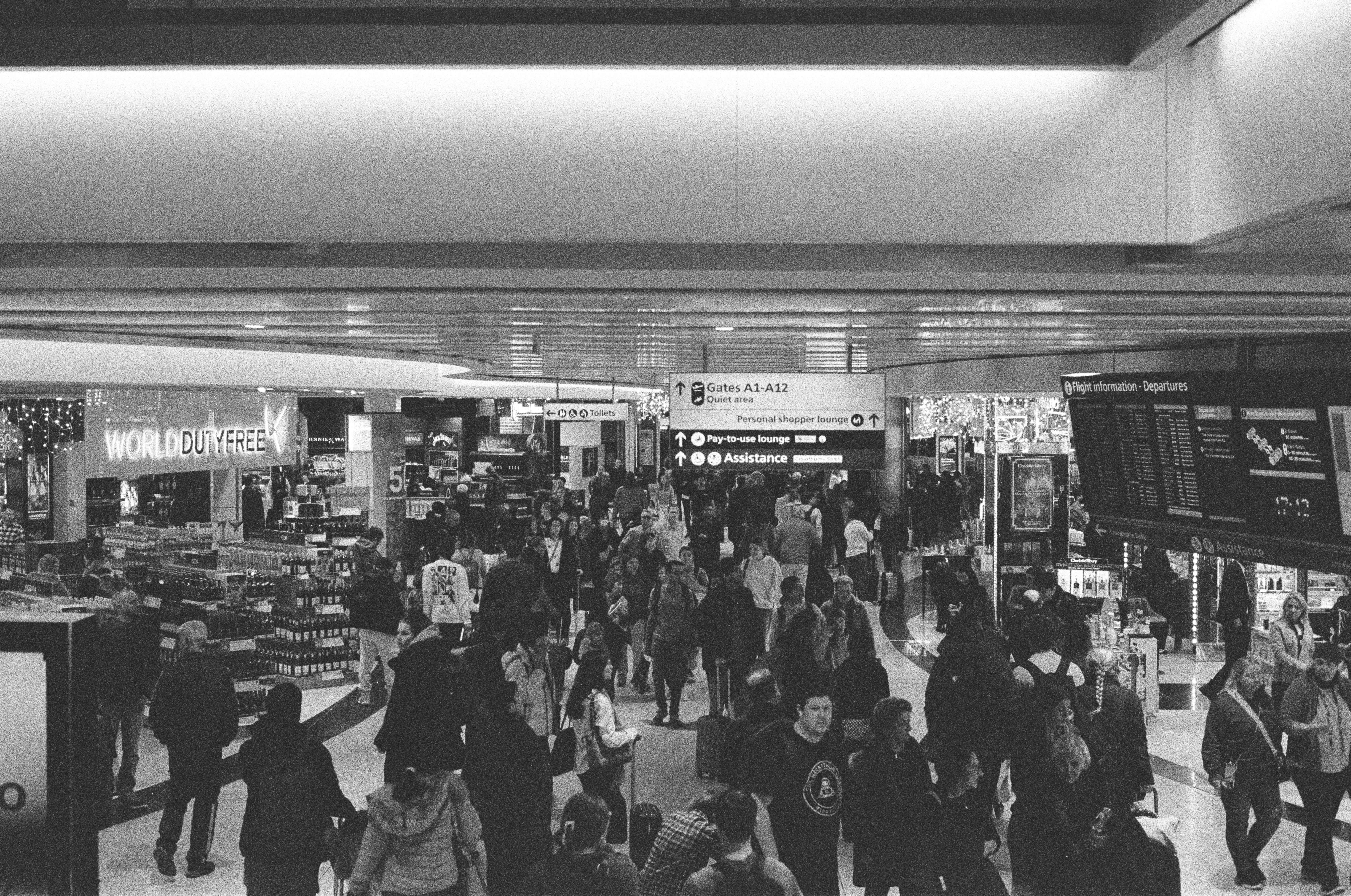 A black and white photo of people at an airport, Black and white photo of a busy airport terminal with many travelers and information boards.