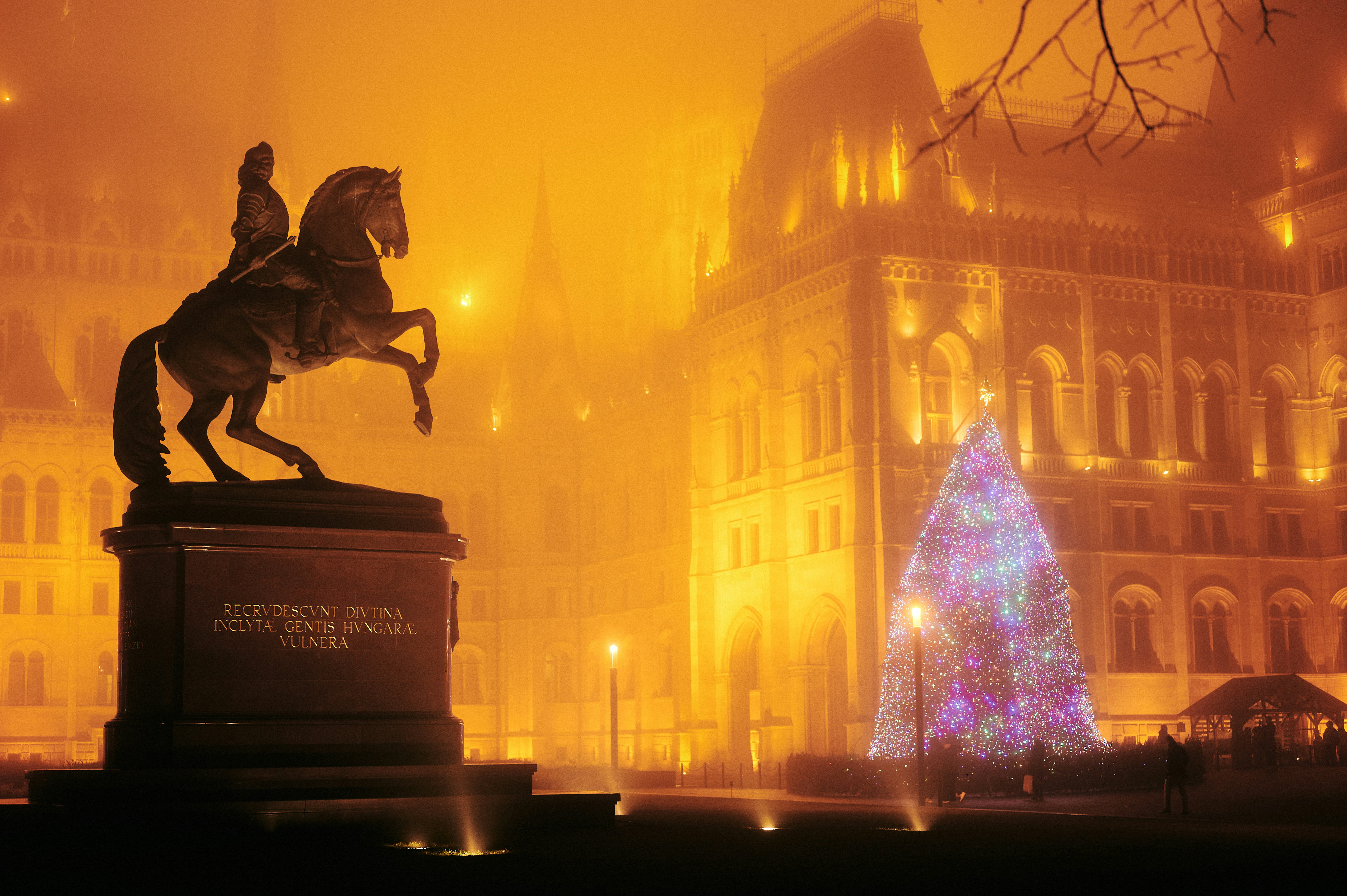 A statue of a man riding a horse in front of a christmas tree