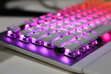A close up of a computer keyboard with purple and red lights