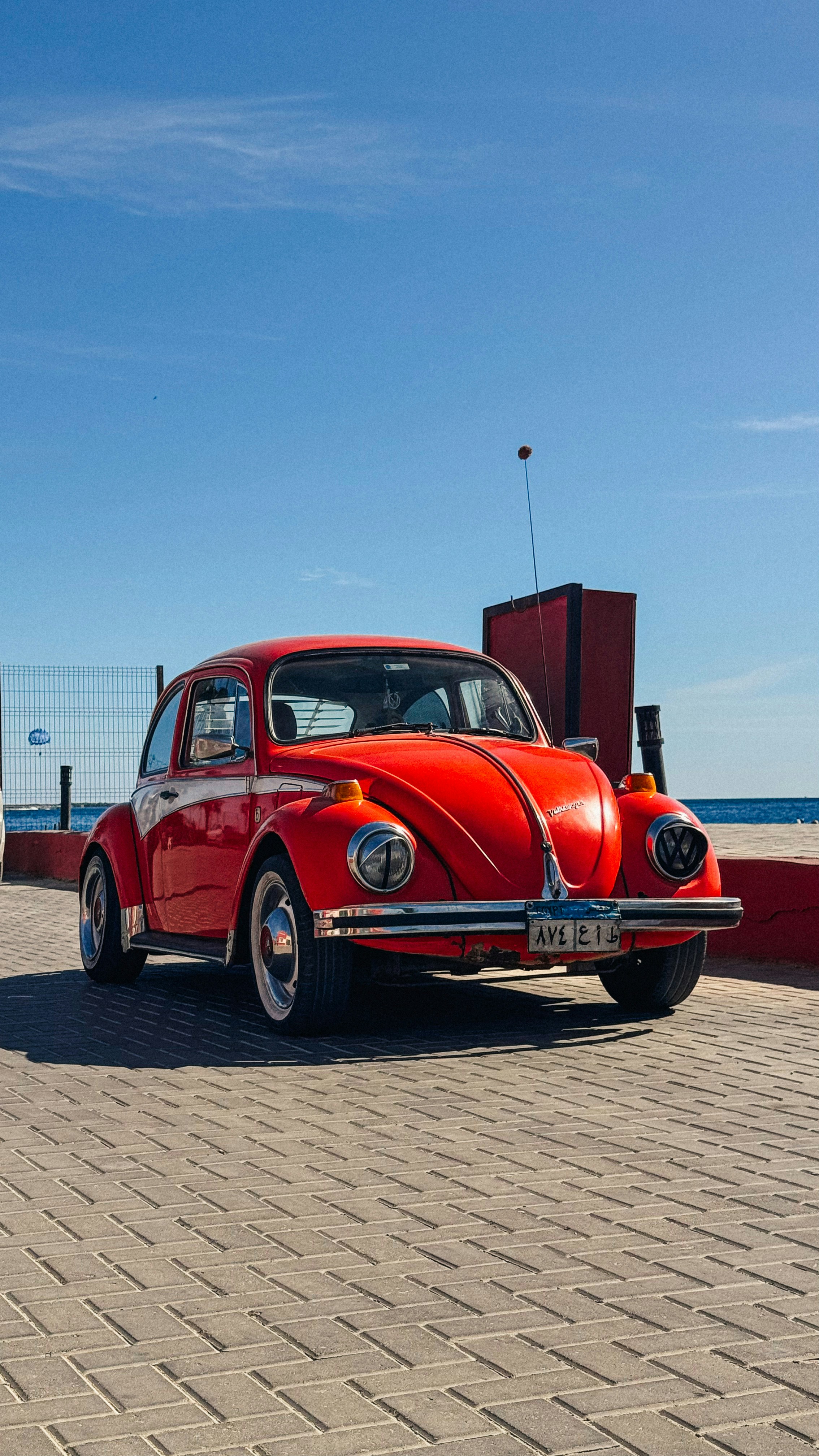 A red car parked on a brick road next to the ocean