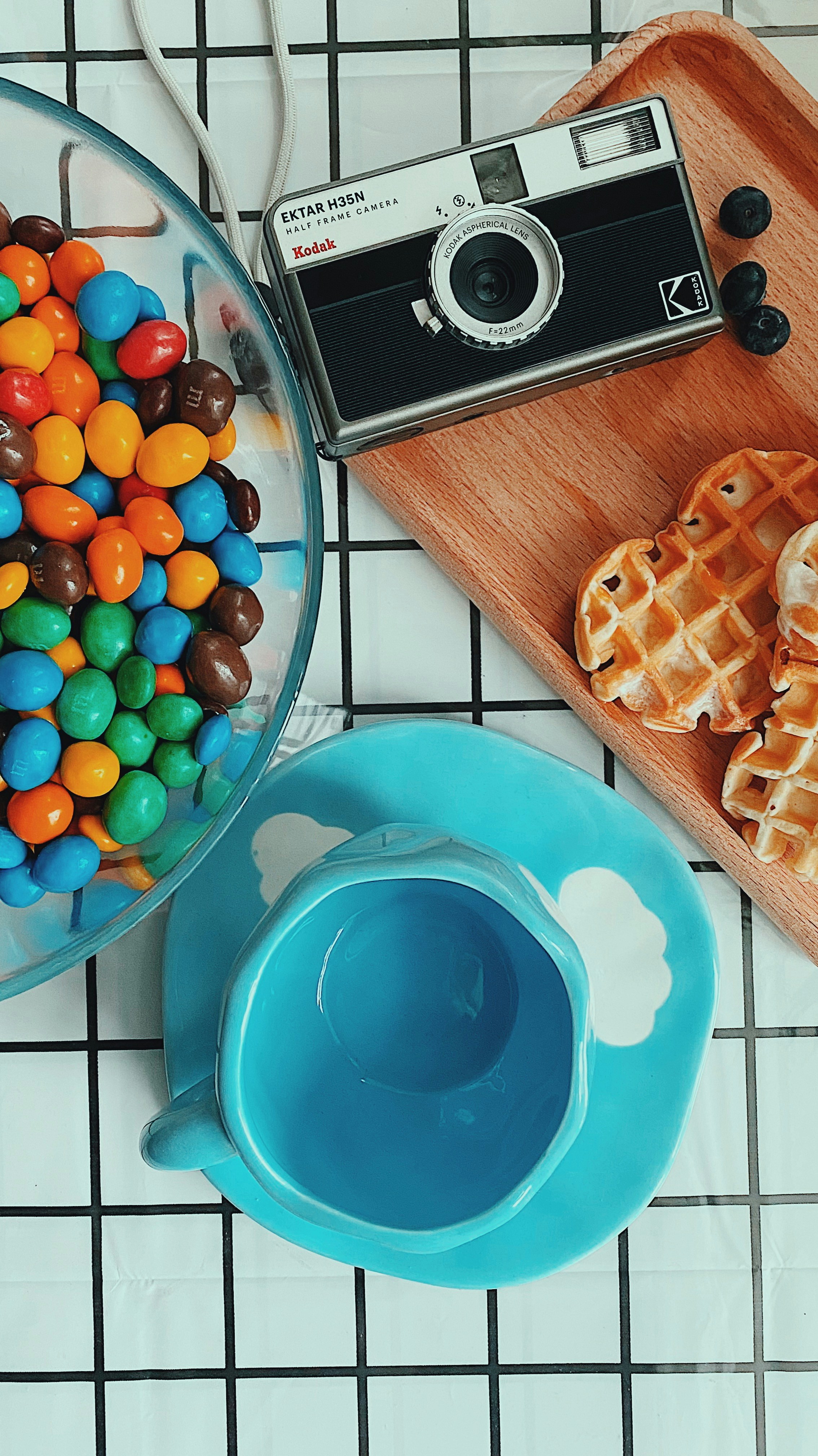 A bowl of jelly beans next to a plate of waffles and a camera