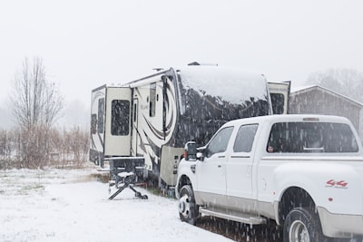 A white truck parked next to a trailer in the snow