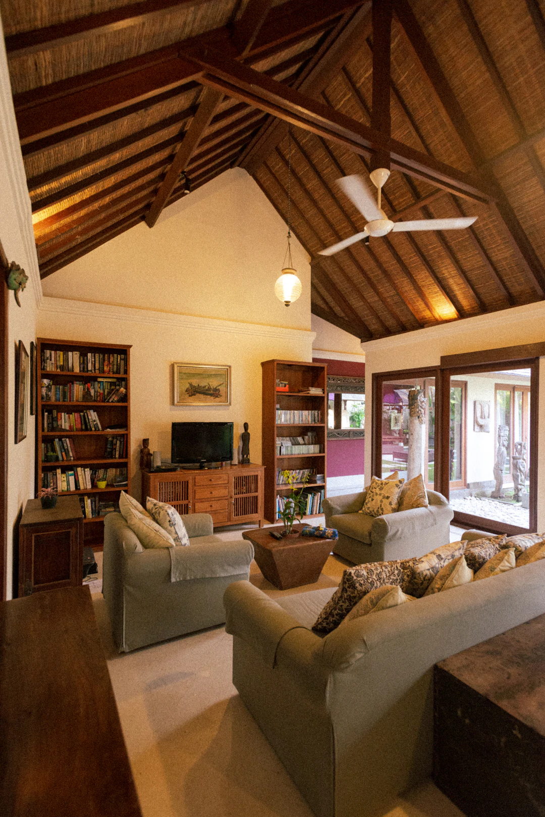 A timber living room with sofas, bookshelves and a ceiling fan