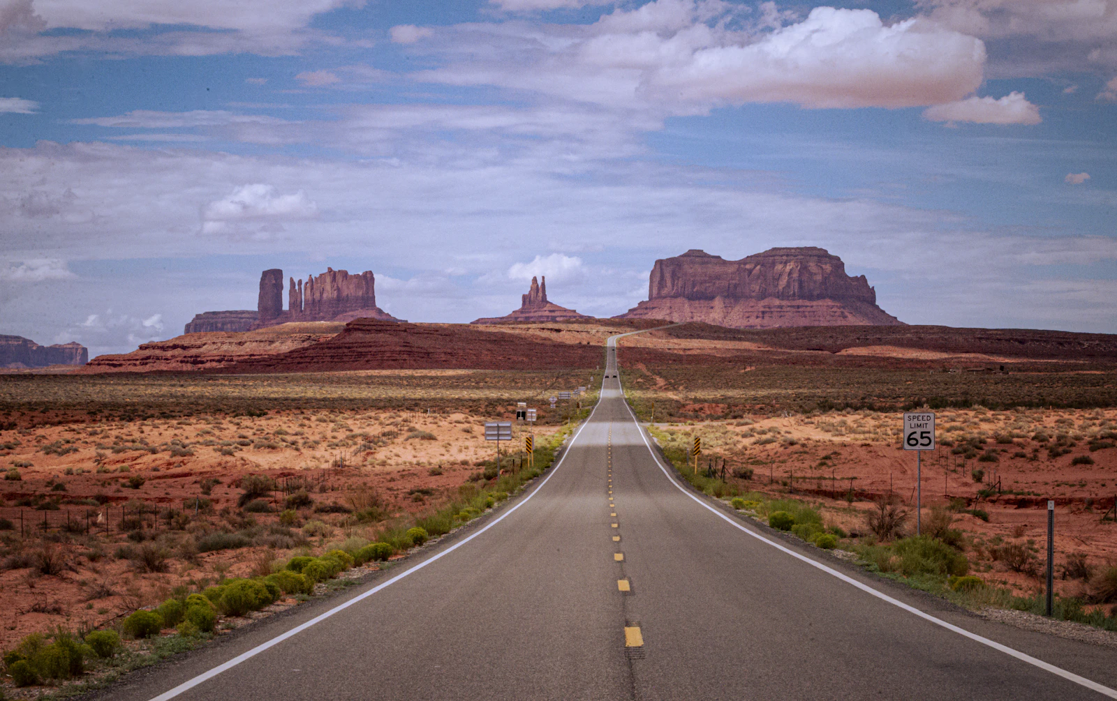 A straight desert highway running to the horizon toward Monument Valley