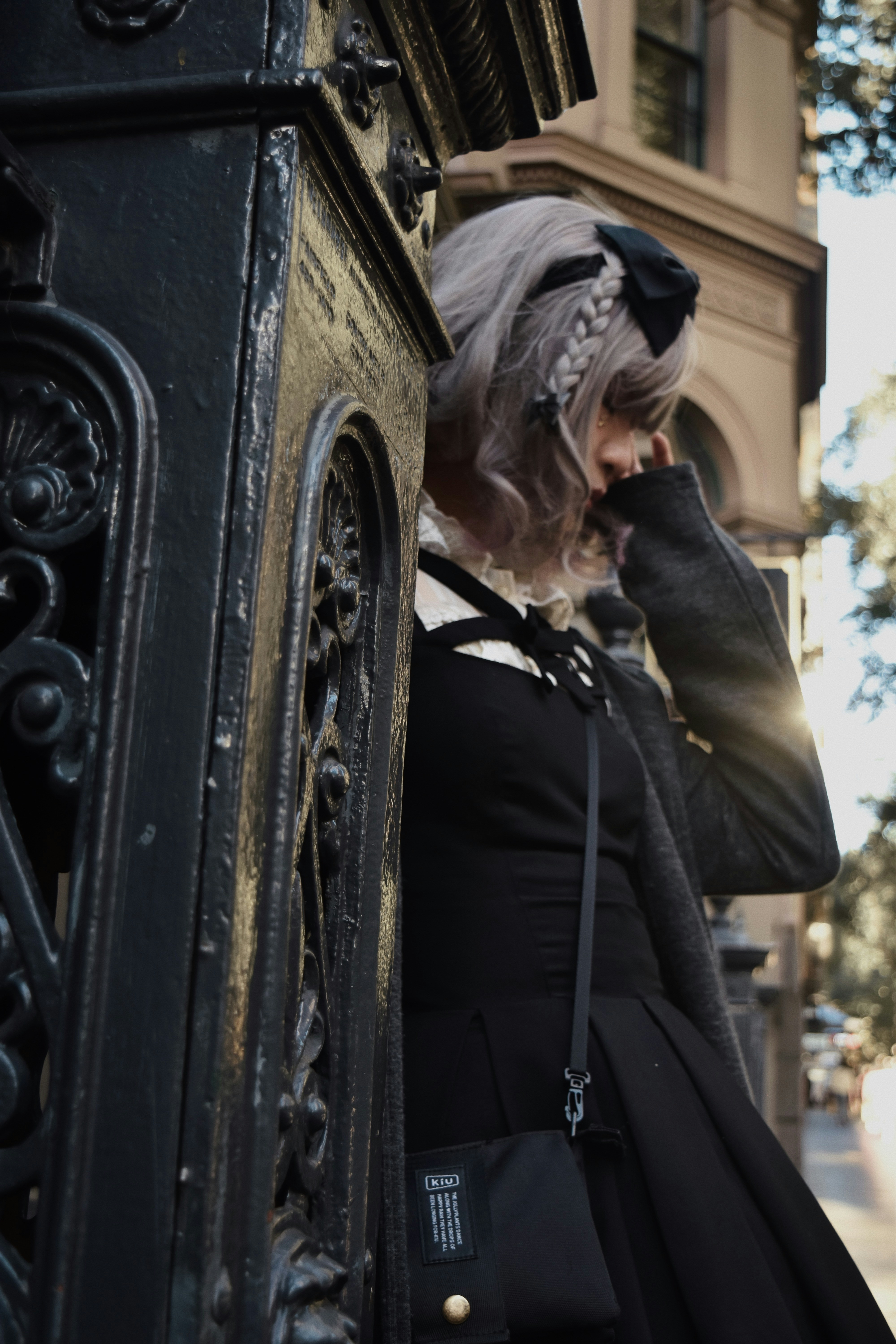 A woman in a black dress is leaning against a fence