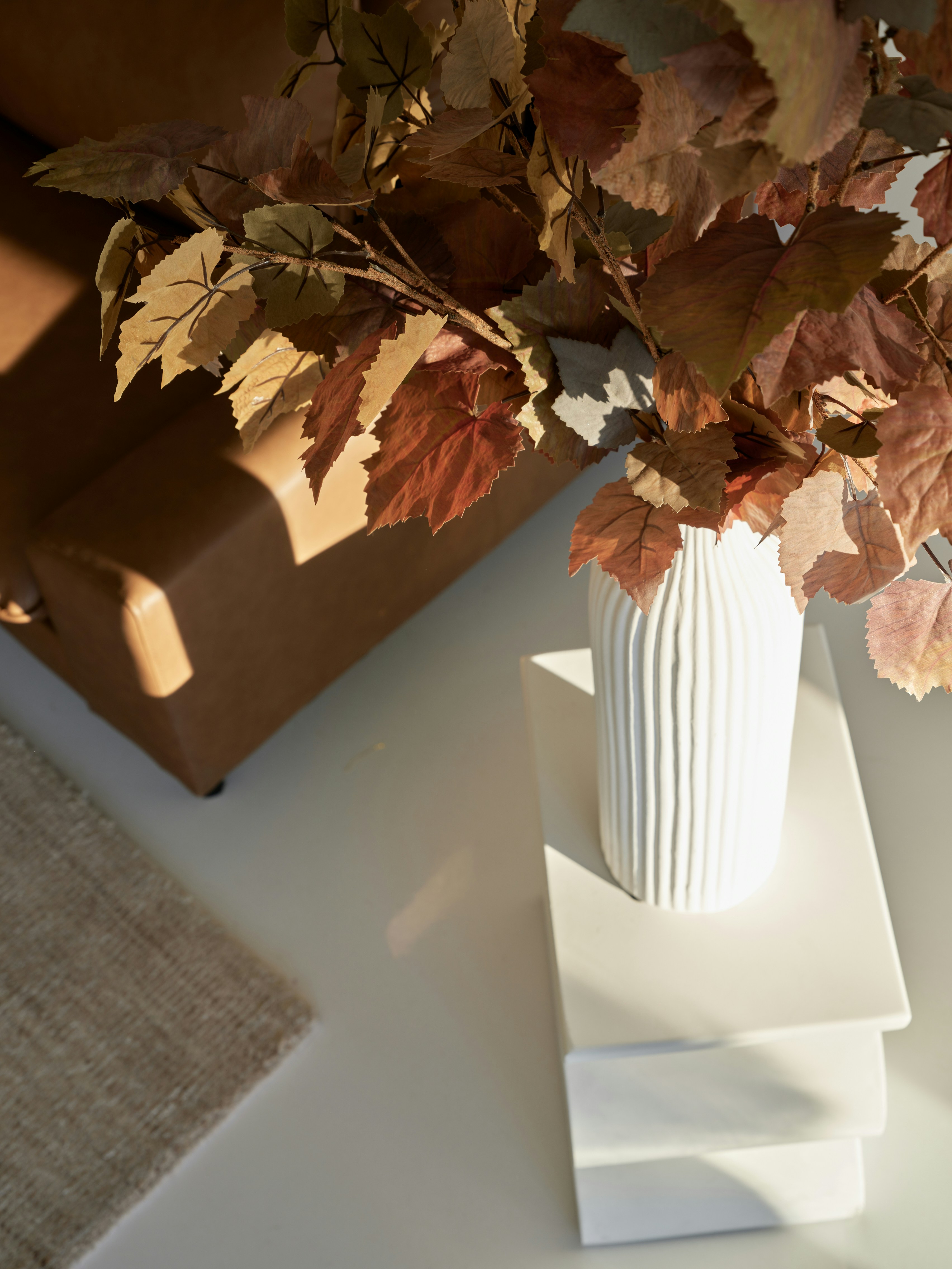 A white vase filled with leaves on top of a table