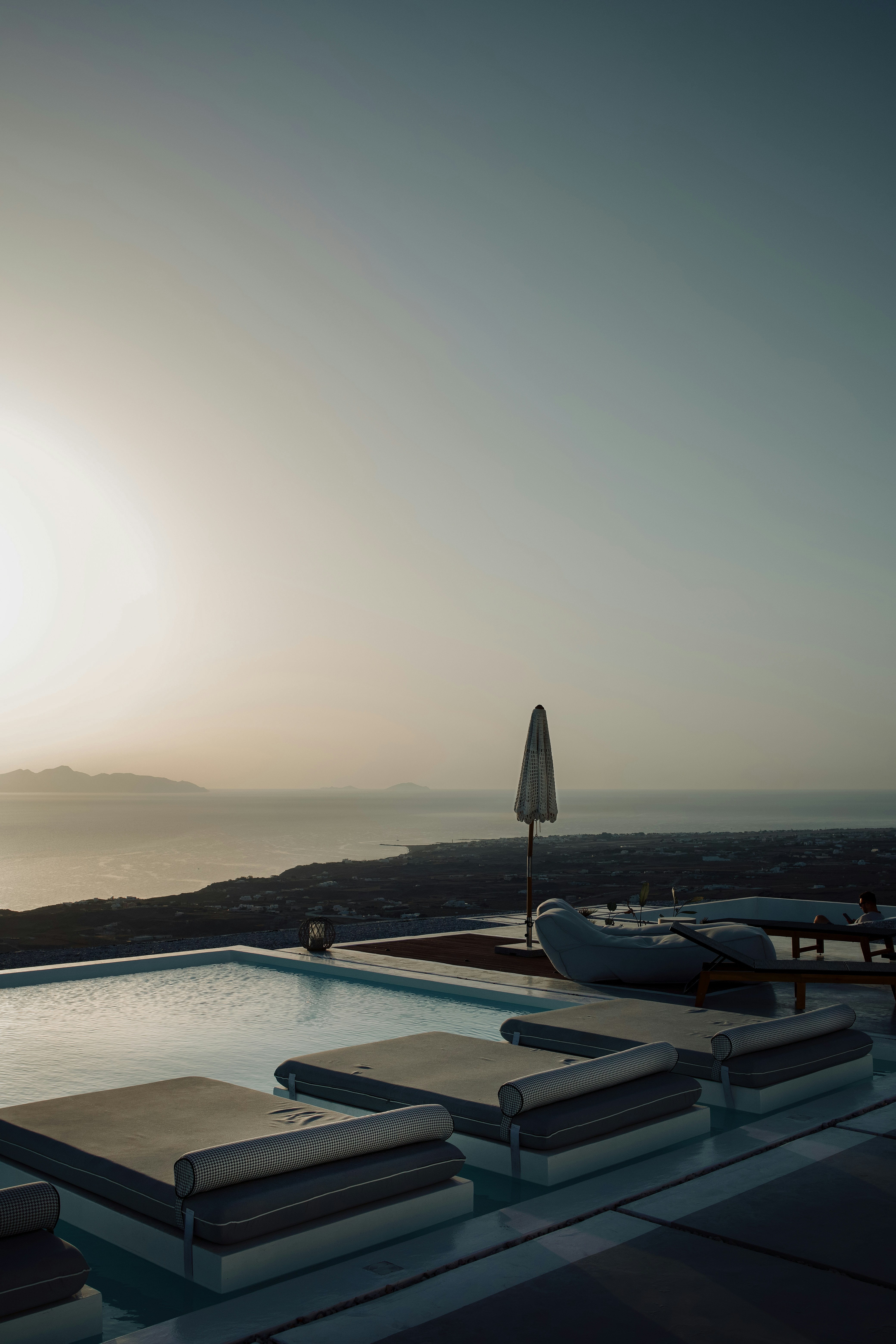 The sun is setting over a pool with lounge chairs
