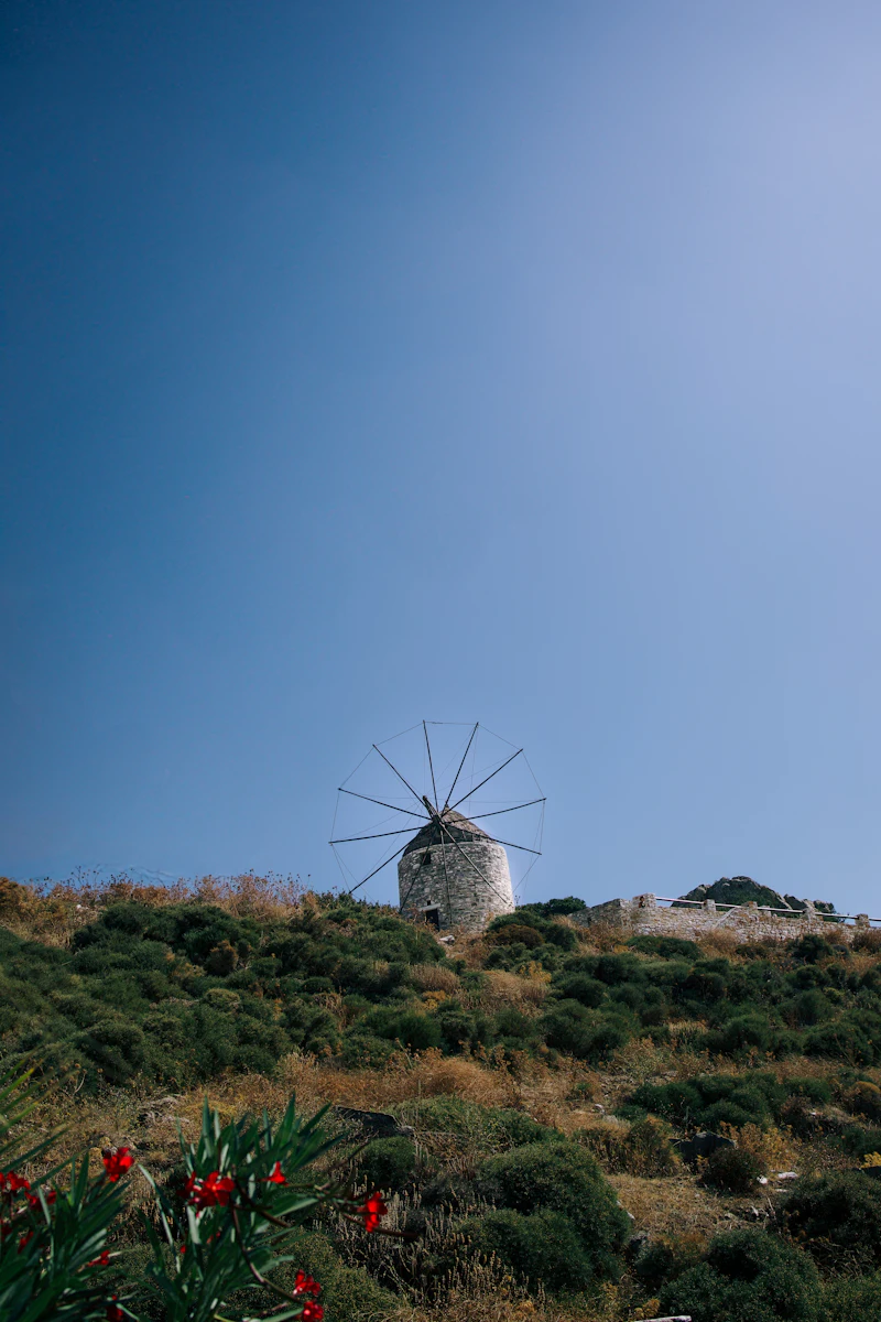 A stone windmill on a green hillside under a clear sky