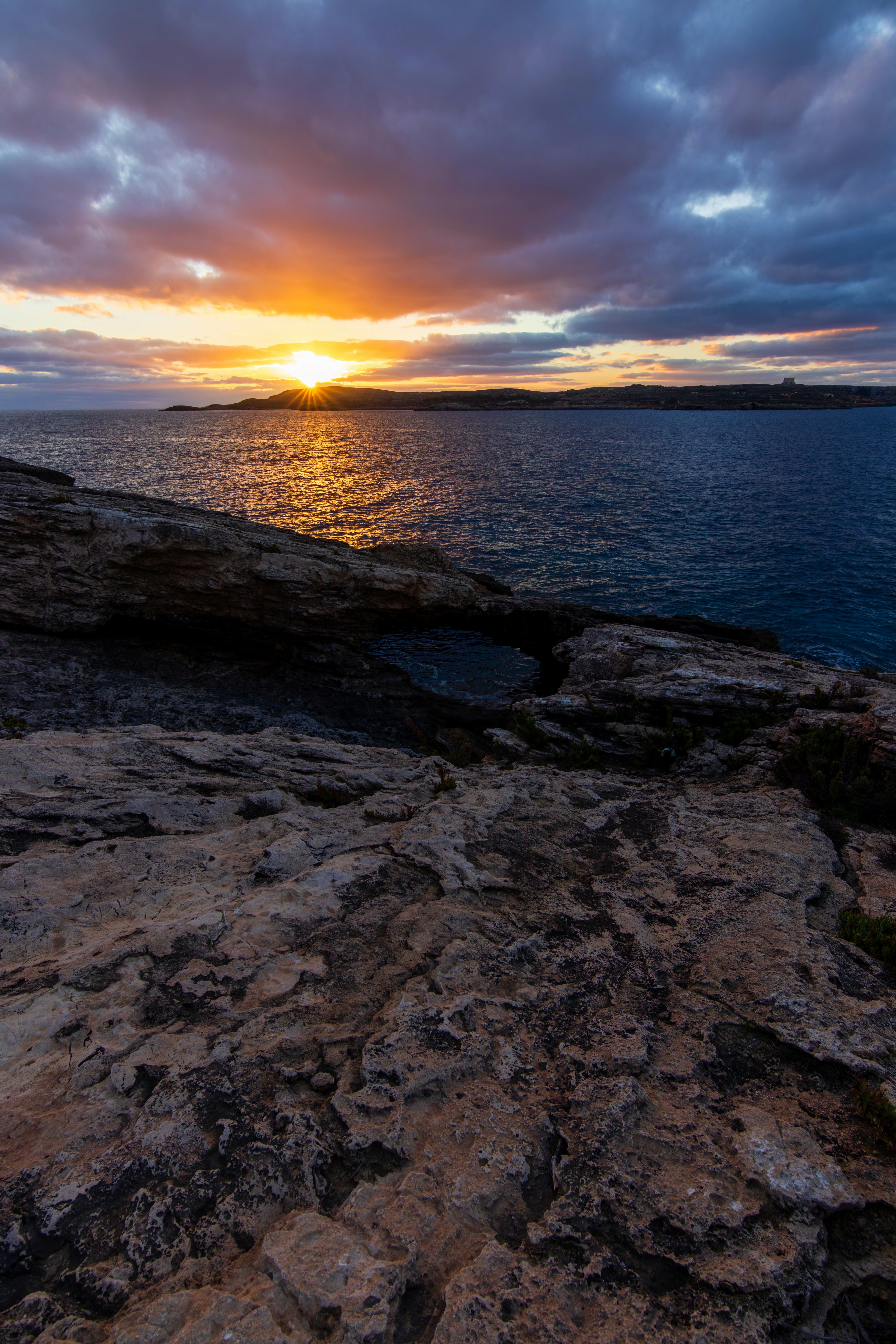 The sun is setting over the ocean on the rocks