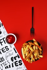 A plate of french fries next to a fork and a bowl of ketchup