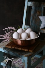 A metal bowl filled with white eggs sitting on top of a wooden table