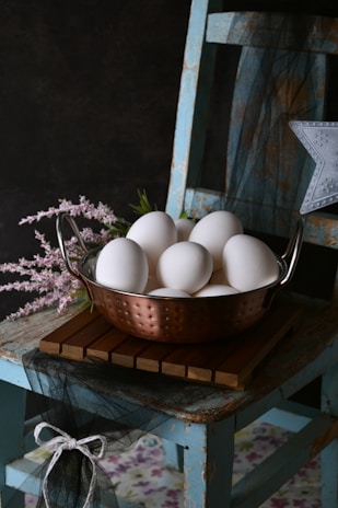 A metal bowl filled with white eggs sitting on top of a wooden table