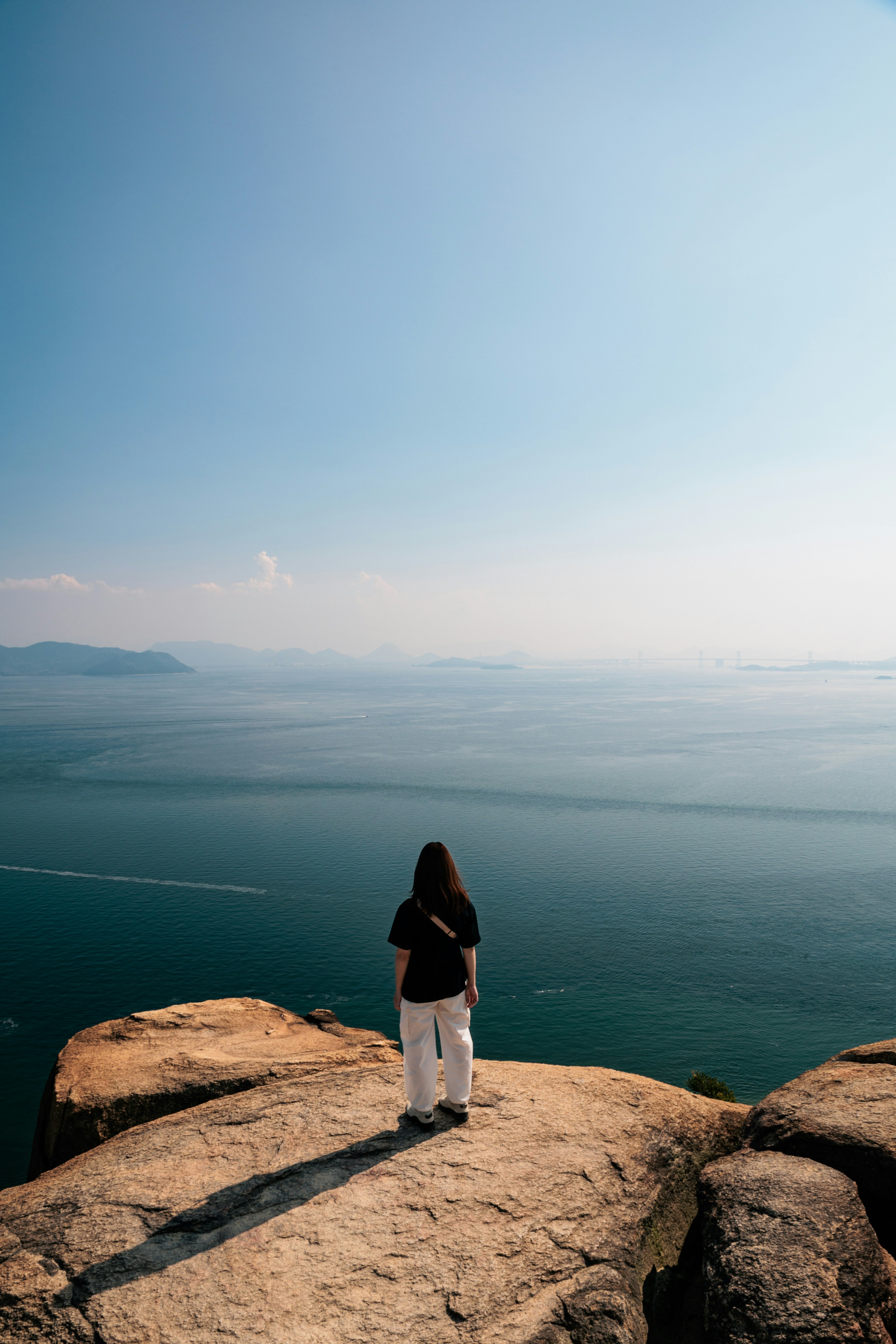 A woman standing on top of a large rock next to the ocean