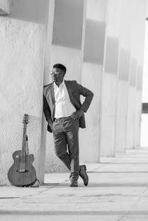 A man leaning against a wall with a guitar