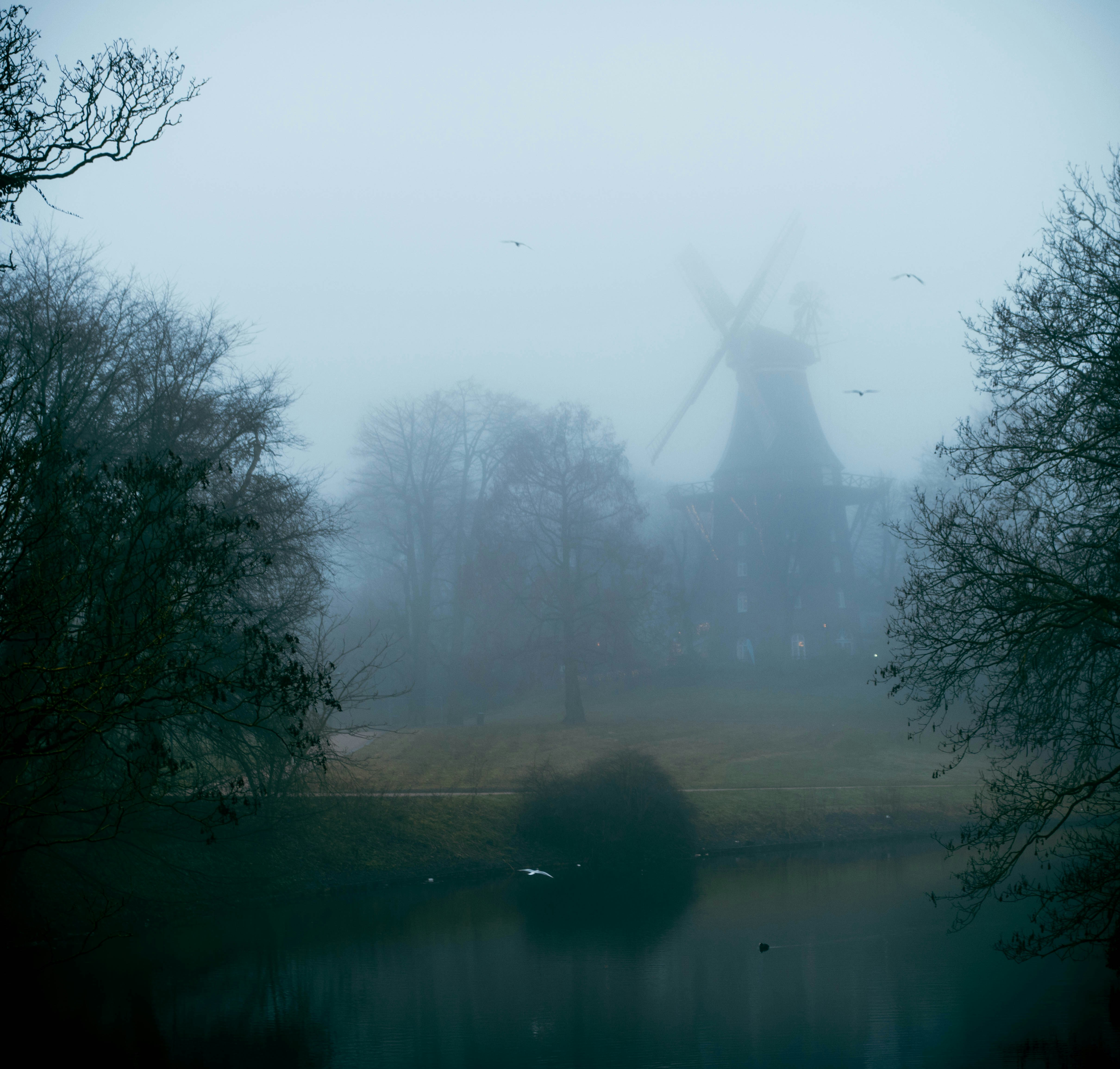 A windmill in a foggy field next to a body of water