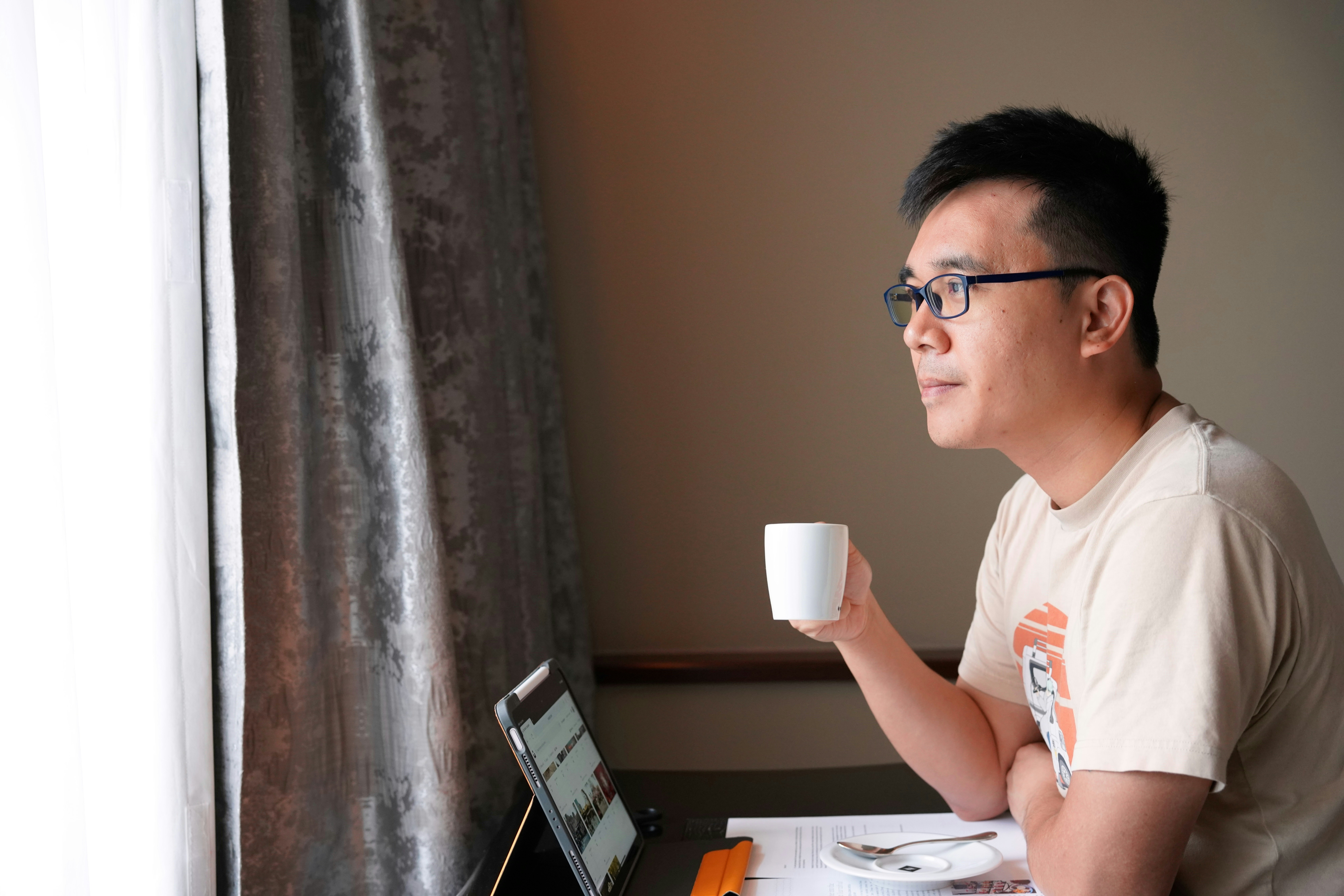 A man sitting at a table with a laptop and a cup of coffee