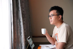 A man sitting at a table with a laptop and a cup of coffee