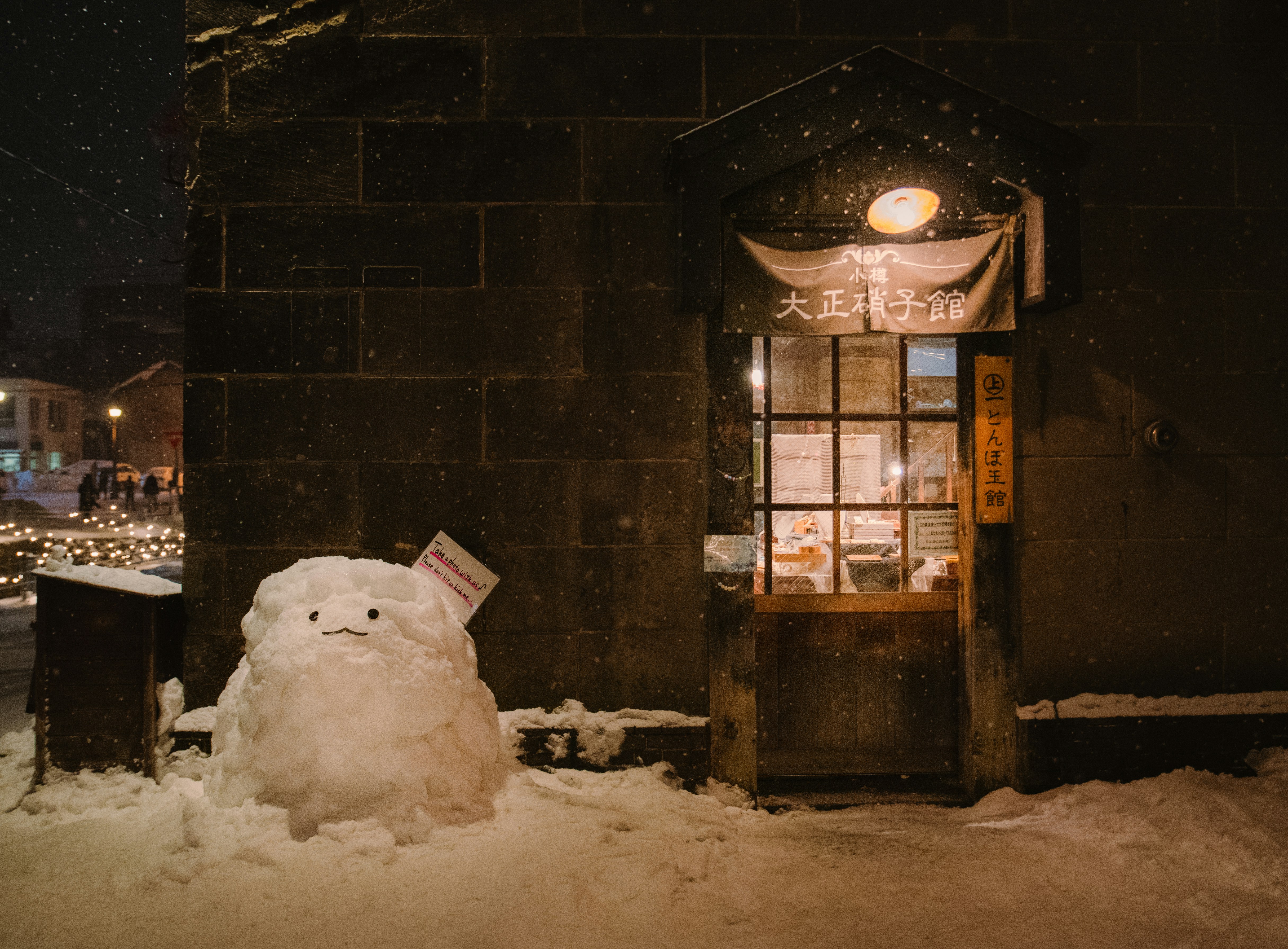 A snowman sitting in front of a building on a snowy night