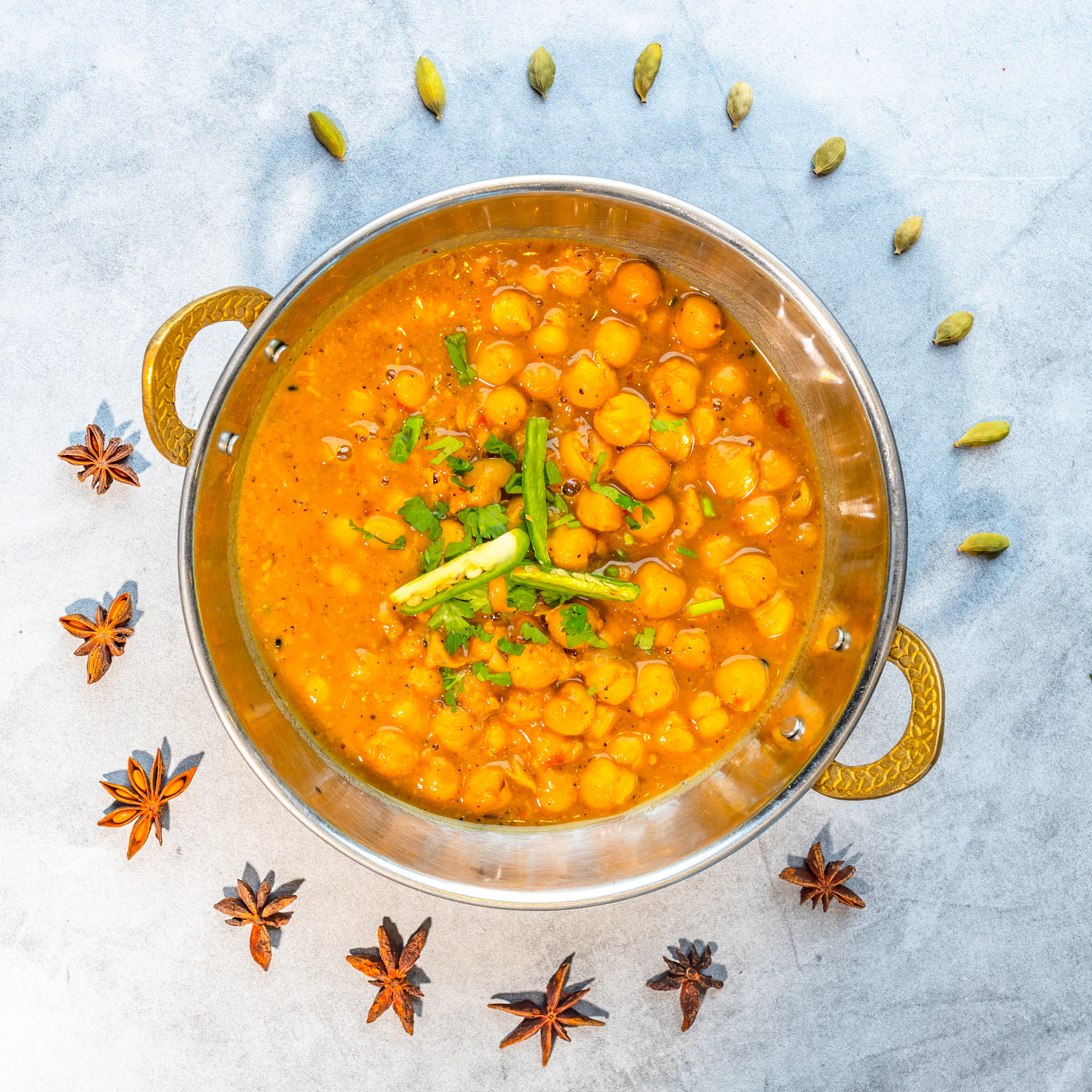 Chana masala in a steel kadai, ringed with cardamom pods and star anise