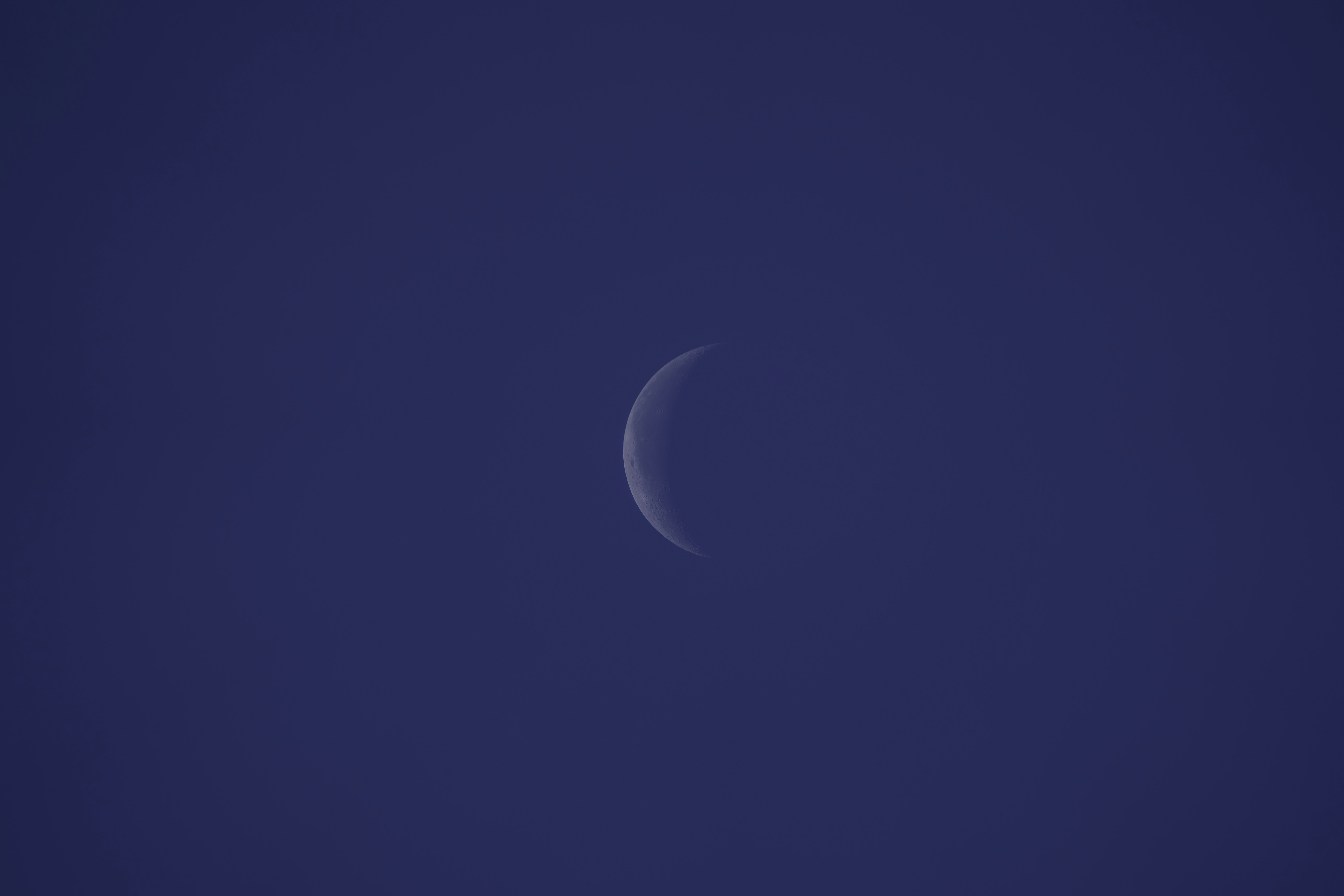 A half moon is seen in the blue sky