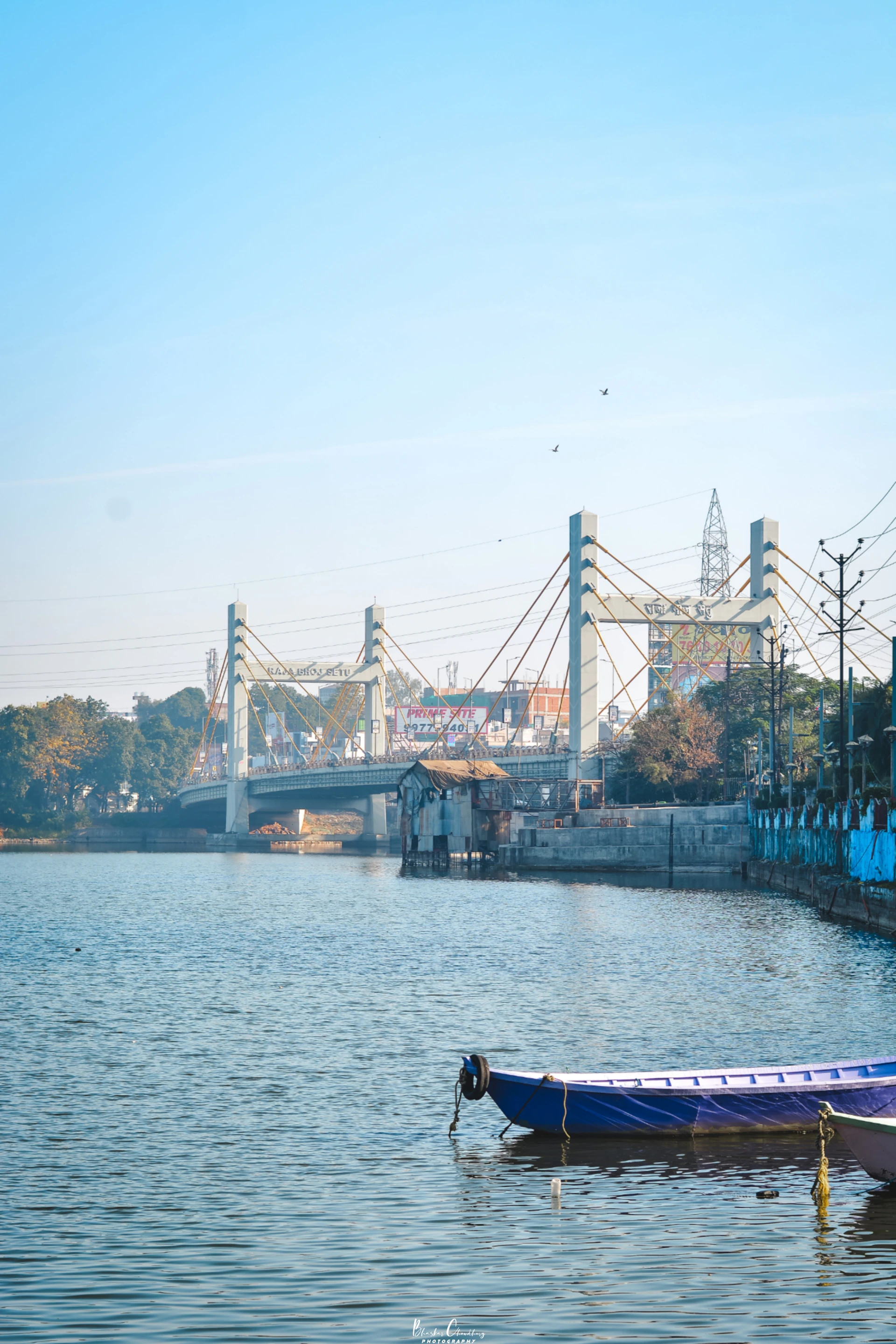 A blue boat floating on top of a river next to a bridge